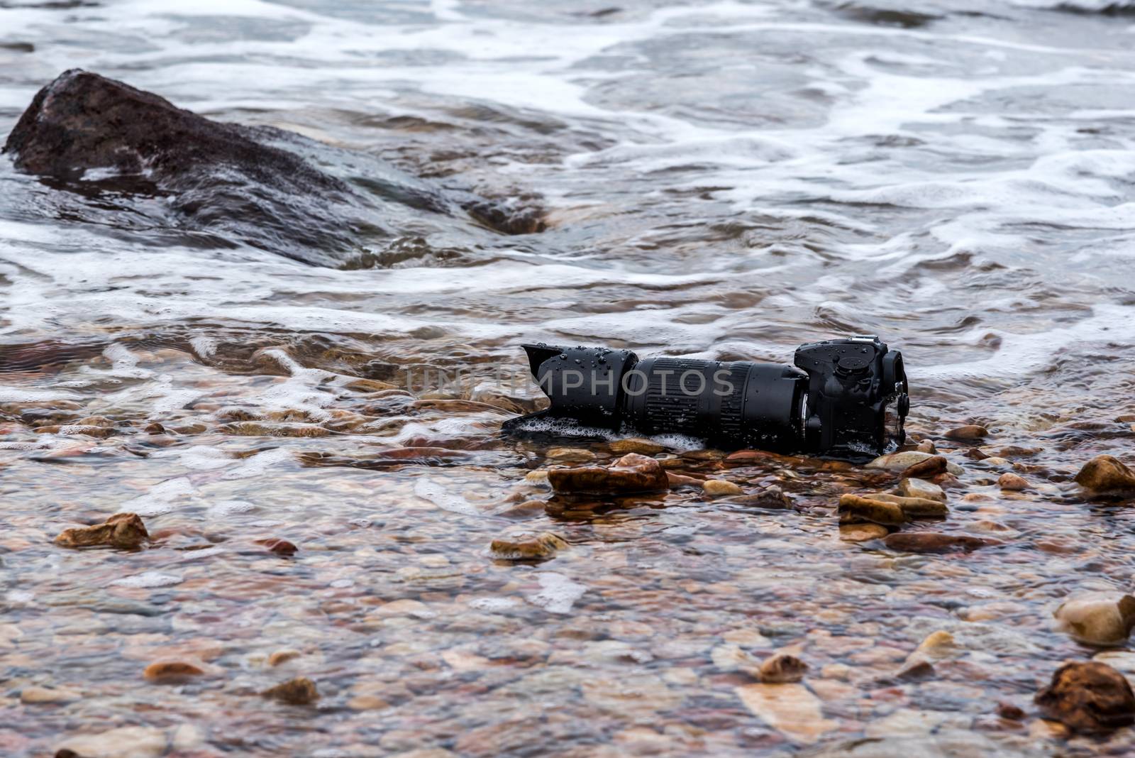 DSLR camera on stone beach wet from water sea wave by PongMoji