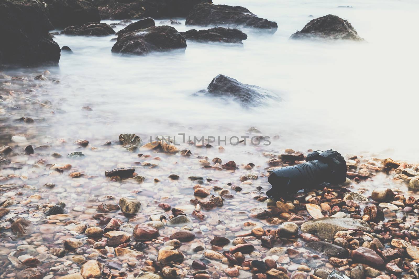 DSLR camera with telephoto lens wet from water sea wave at stone beach when travel and test using in the extreme environment demo waterproof by photographer