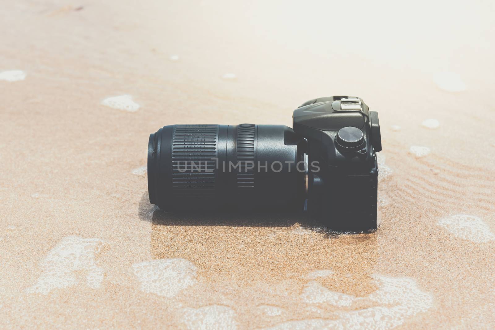 DSLR camera with telephoto lens on a beach it wet from water sea wave when travel and test using in the extreme environment demo waterproof by photographer