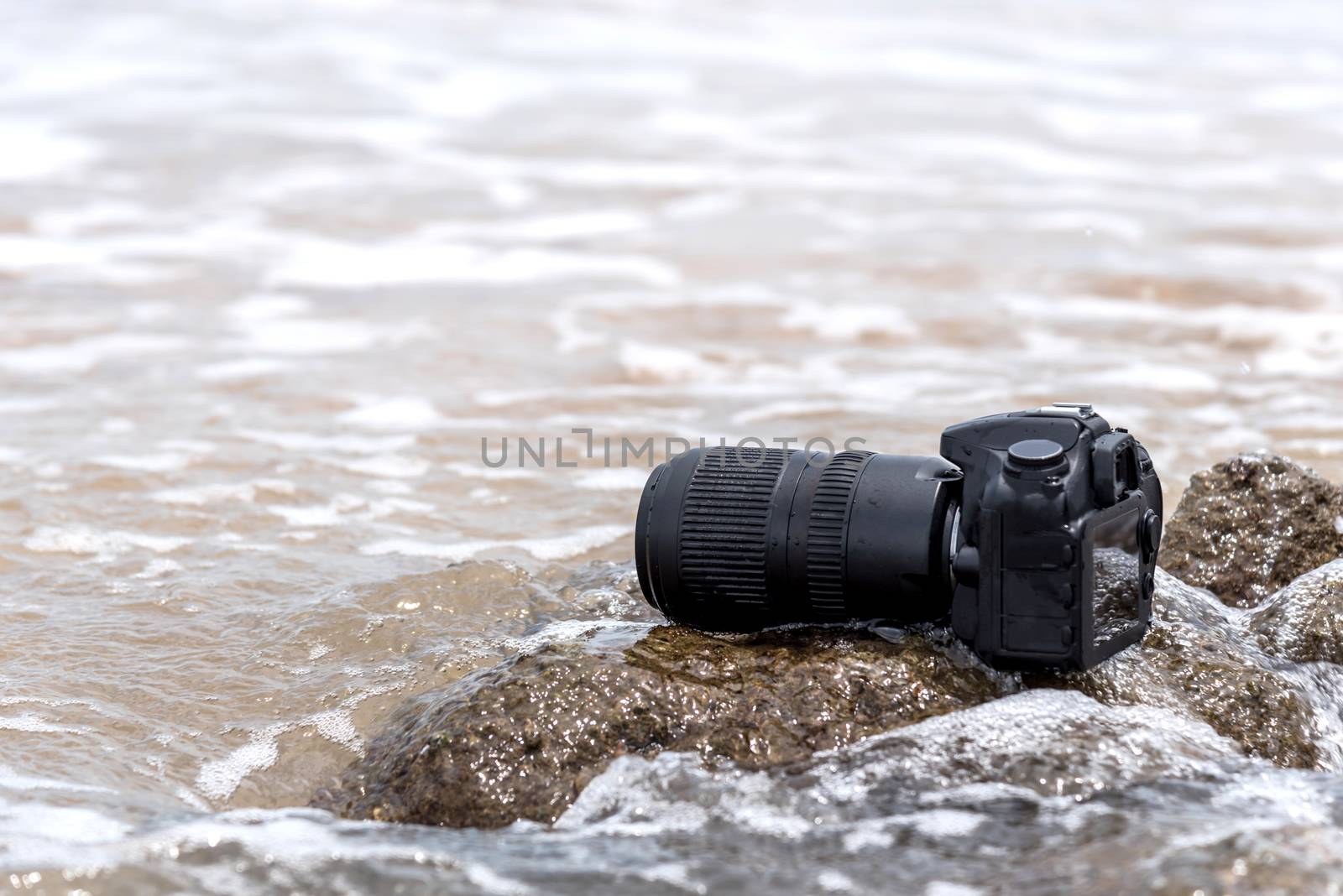 DSLR camera on stone beach wet from water sea wave by PongMoji