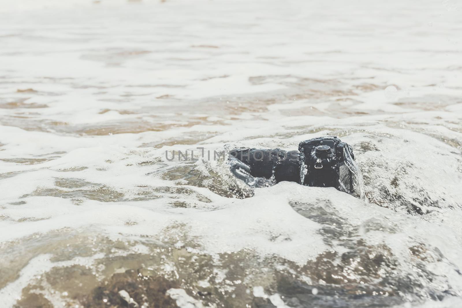 DSLR camera on stone beach wet from water sea wave by PongMoji