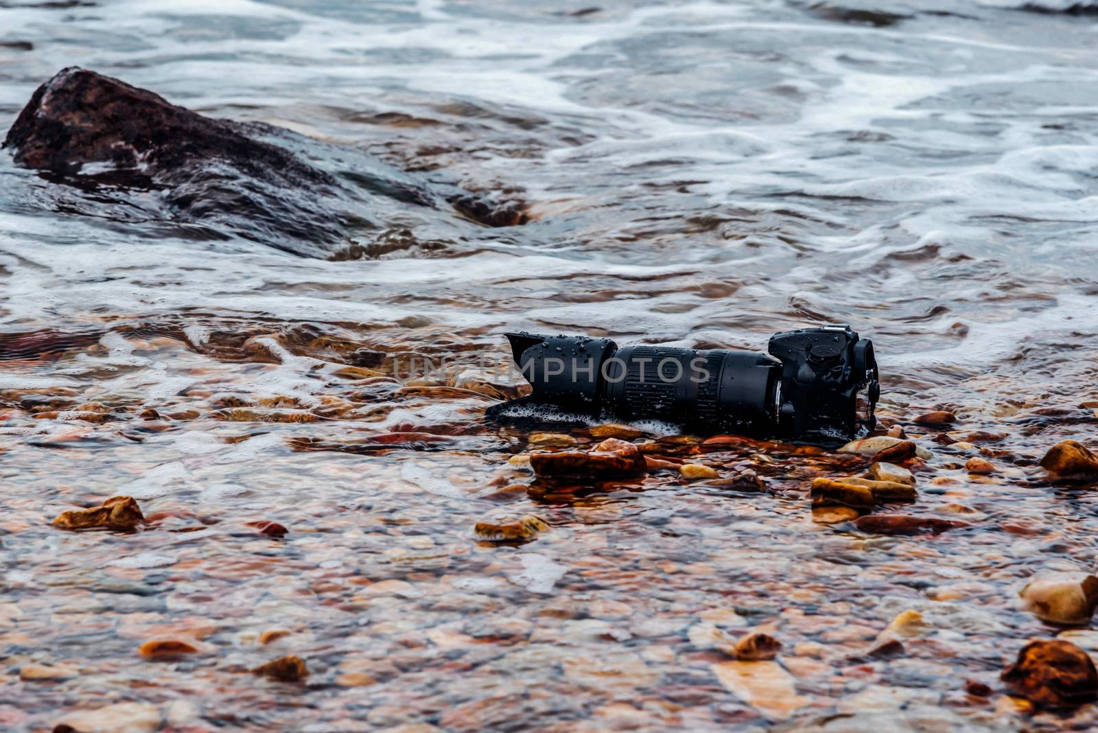 DSLR camera with telephoto lens wet from water sea wave at stone beach when travel and test using in the extreme environment demo waterproof by photographer