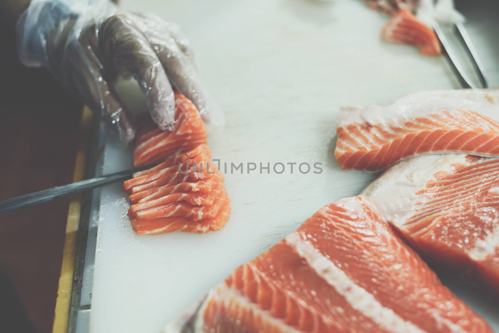 Asian chef slice salmon by knife on boad for japanese food delicacy consisting sashimi salmon of very fresh raw salmon fish sliced into thin pieces serving with radish sliced in japanese restaurant