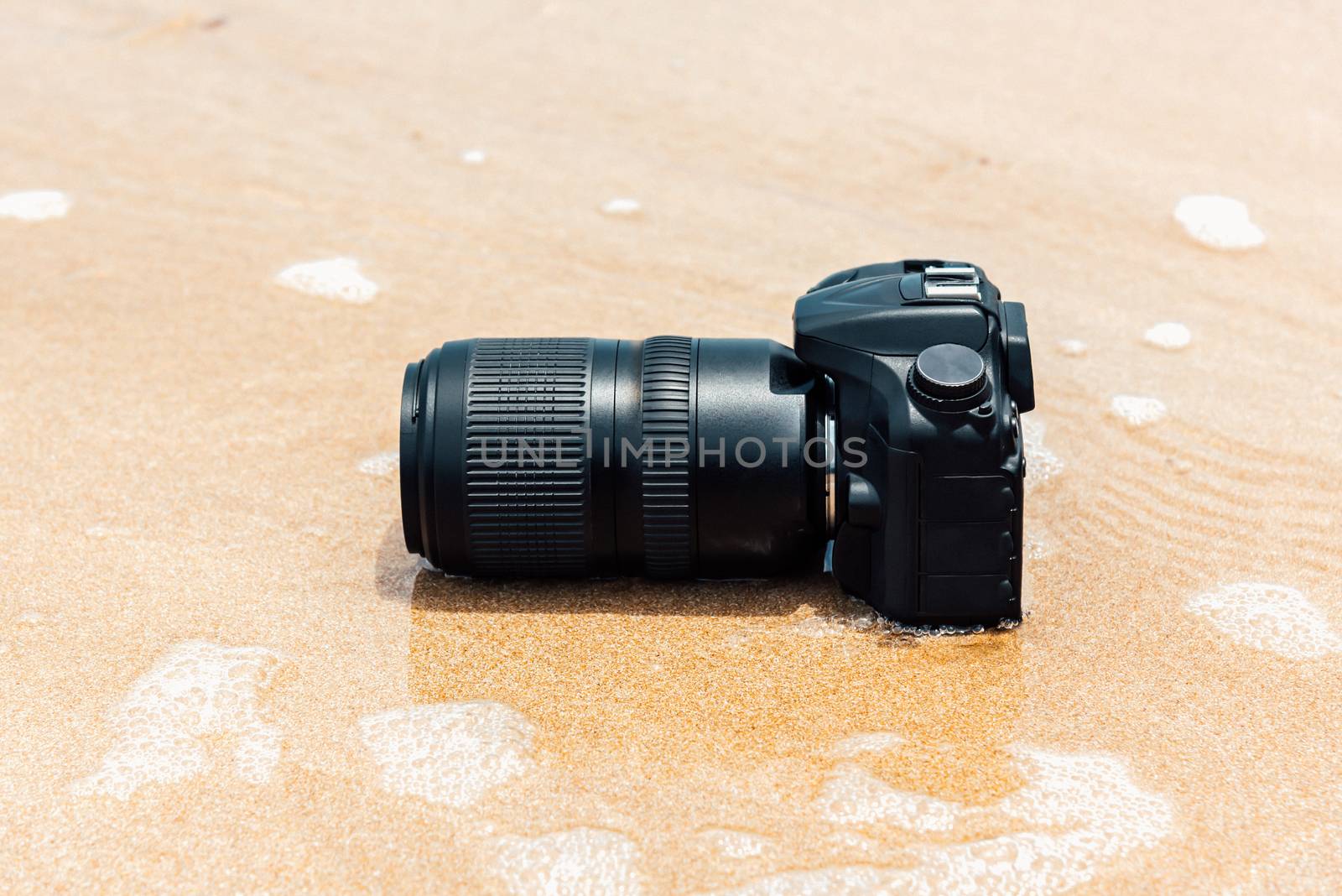 DSLR camera on beach wet from water sea wave by PongMoji