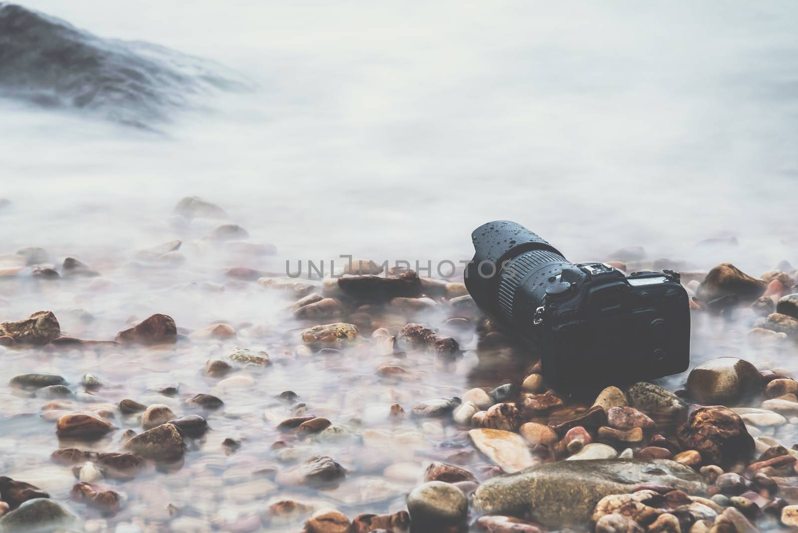 DSLR camera with telephoto lens wet from water sea wave at stone beach when travel and test using in the extreme environment demo waterproof by photographer