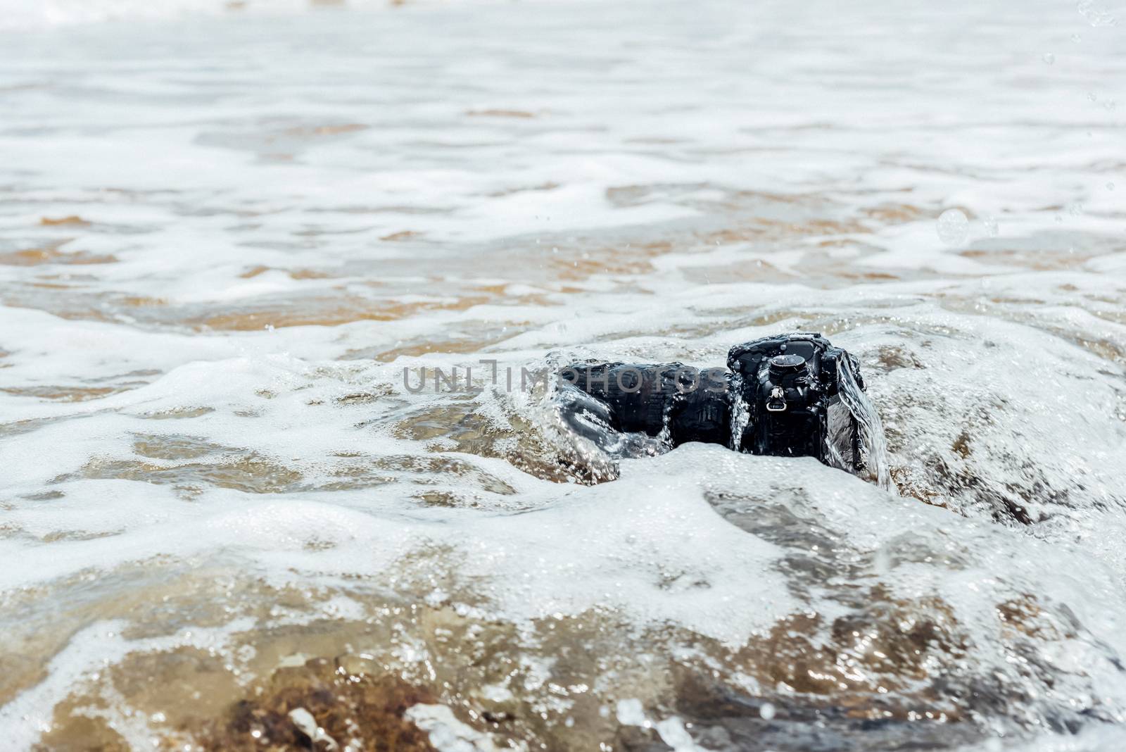 DSLR camera with telephoto lens wet from water sea wave at stone beach when travel and test using in the extreme environment demo waterproof by photographer