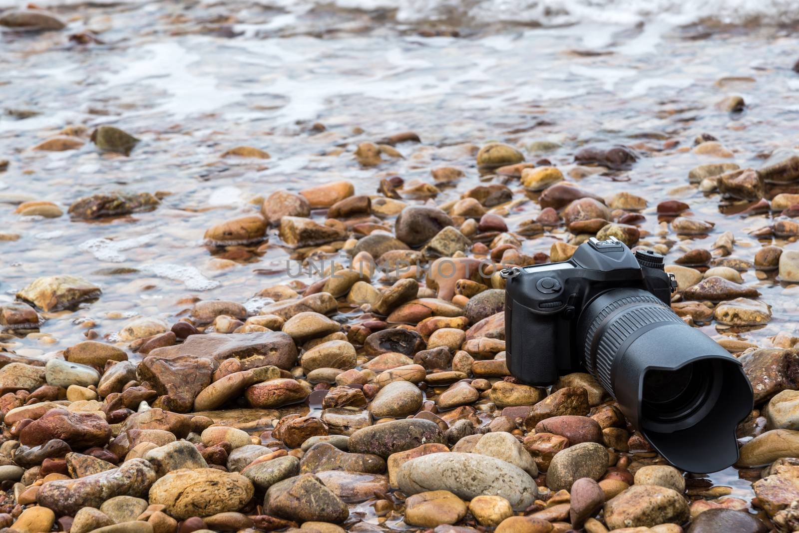 DSLR camera on stone beach wet from water sea wave by PongMoji