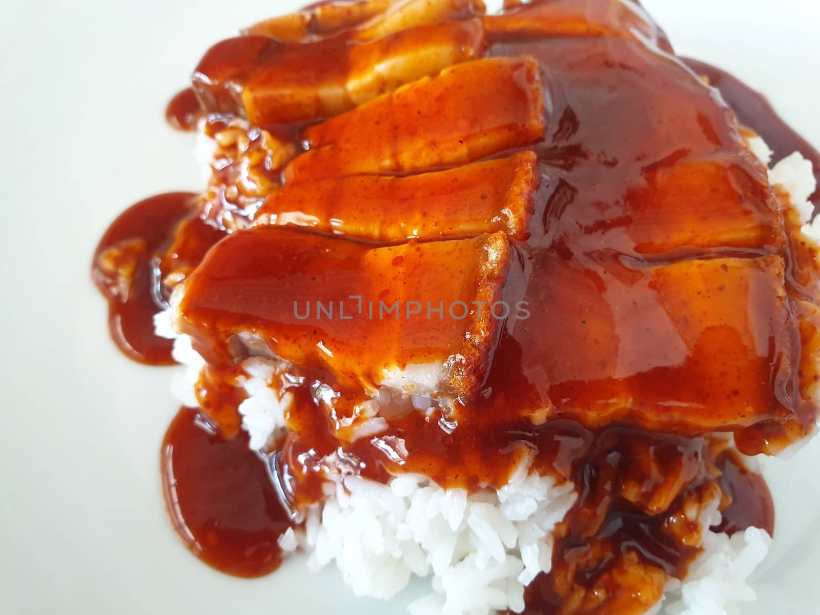 Barbecued red pork in sauce with rice and cucumber served in dish on wood table in Thai restaurant at Thai street food market at Bangkok Thailand