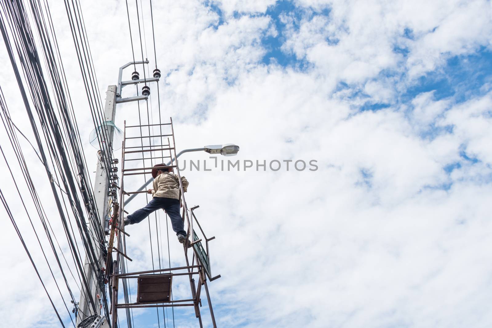 Electricians or handyman or worker risk working to install electric line on high pole by scaffolding on pickup truck at Bangkok Thailand.