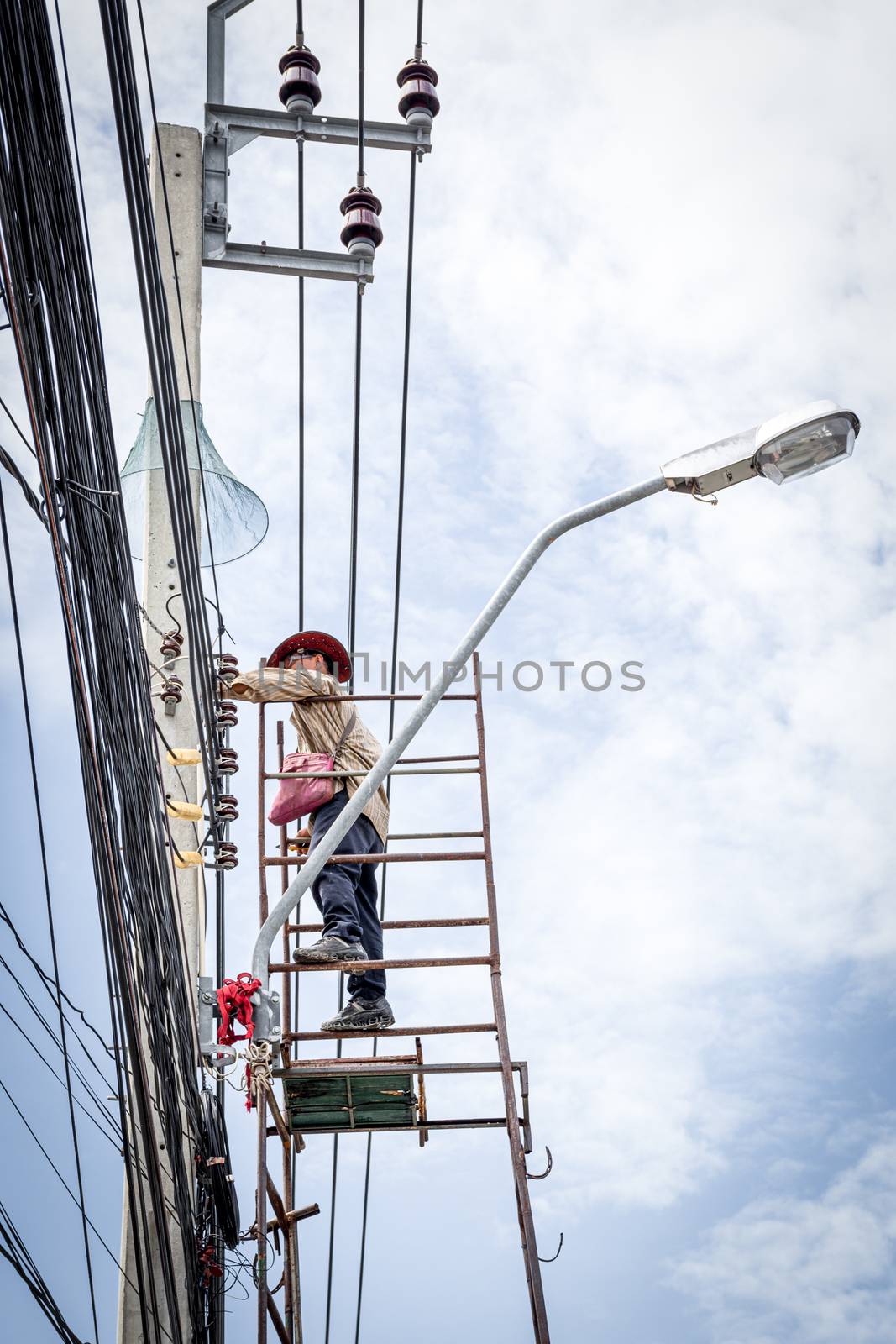 Electricians or handyman or worker risk working to install electric line on high pole by scaffolding on pickup truck at Bangkok Thailand.