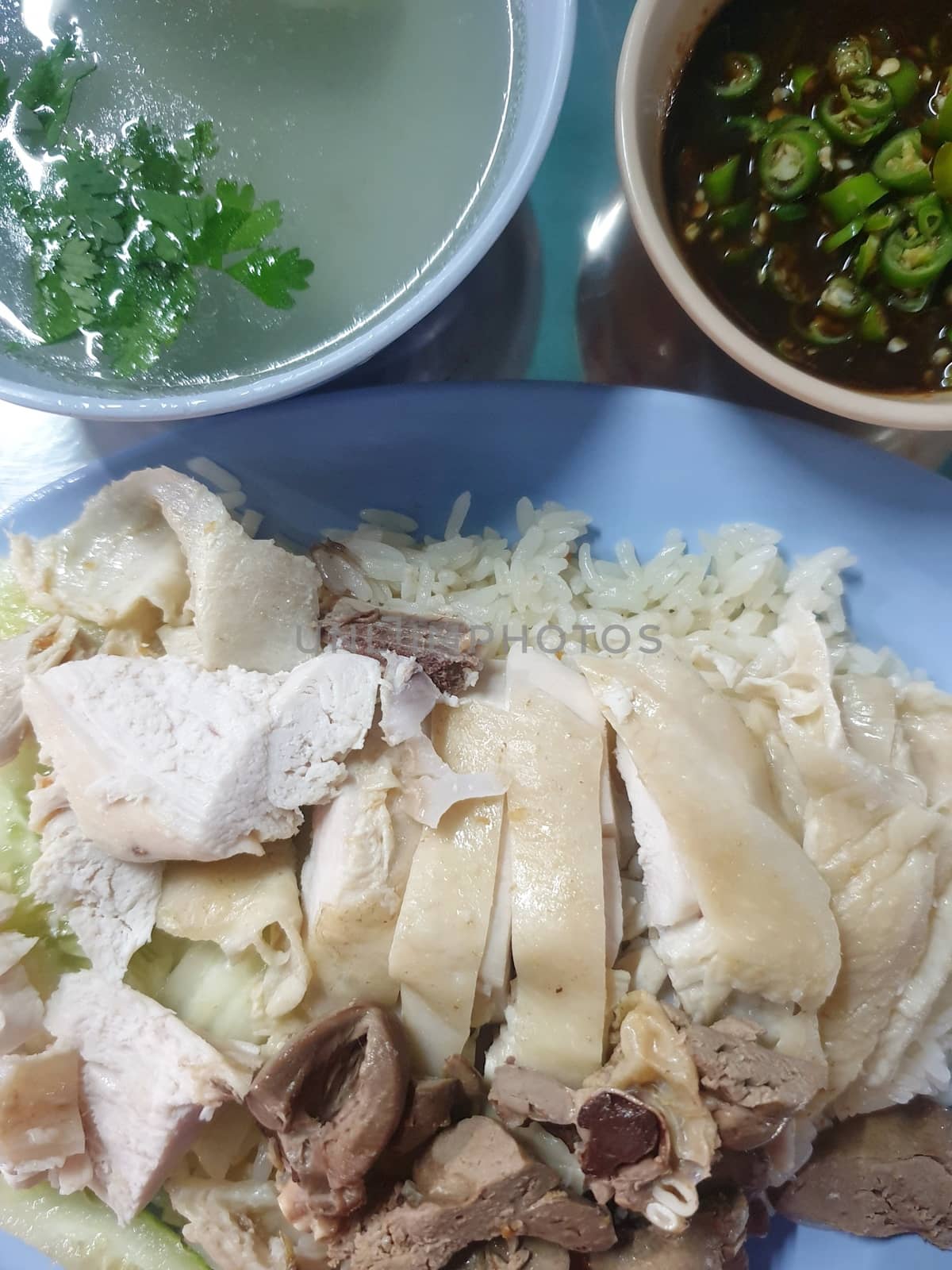 Rice steamed with chicken soup (hainanese chicken rice) with cucumber, liver and sauce for sale at Thai street food market or restaurant in Bangkok Thailand