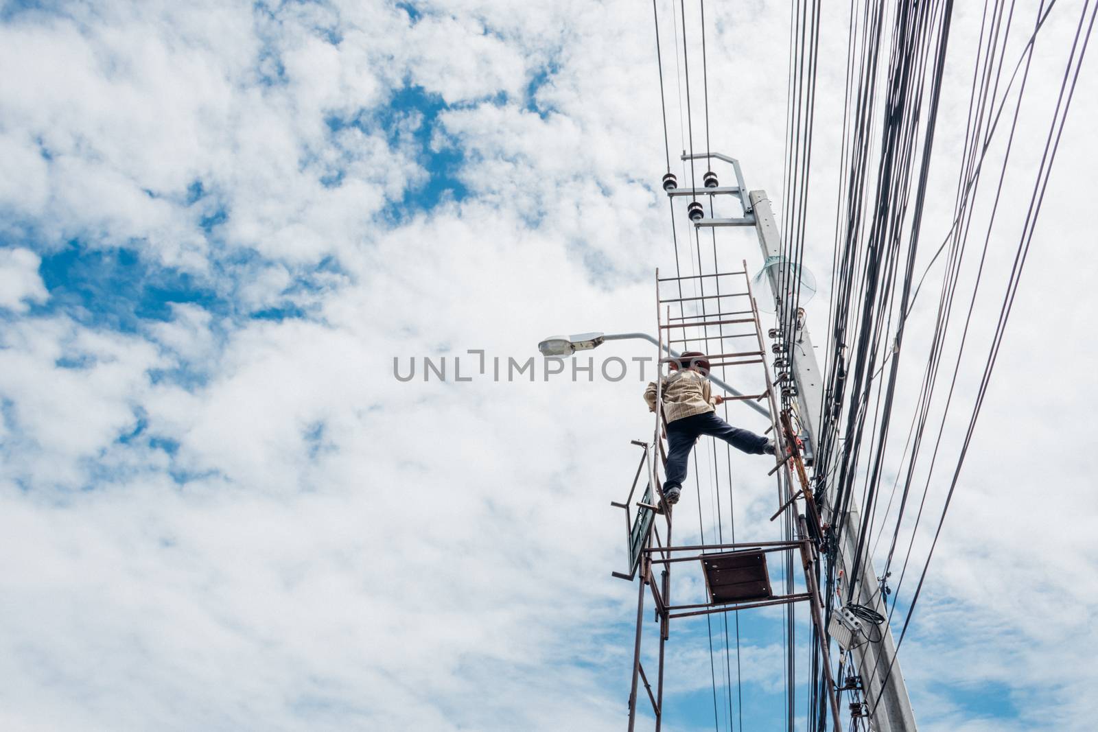 Electricians or handyman or worker risk working to install electric line on high pole by scaffolding on pickup truck at Bangkok Thailand.