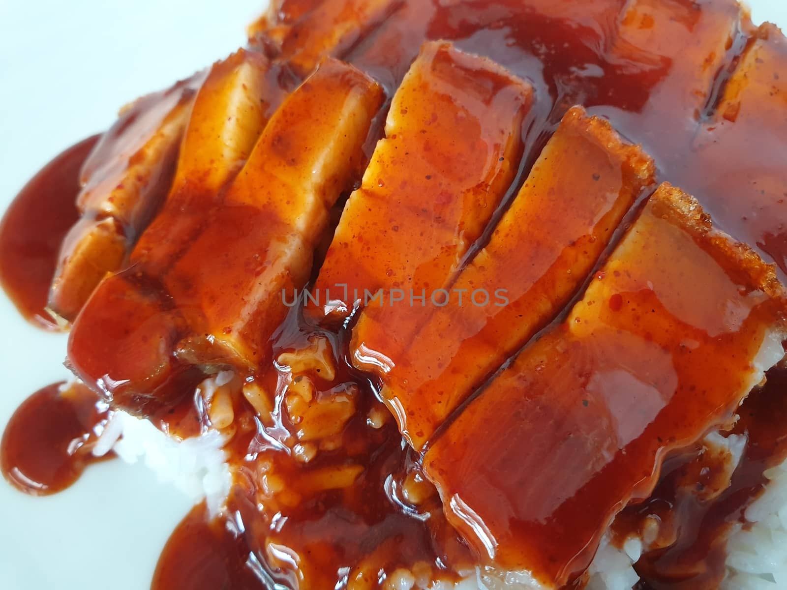 Barbecued red pork in sauce with rice and cucumber served in dish on wood table in Thai restaurant at Thai street food market at Bangkok Thailand