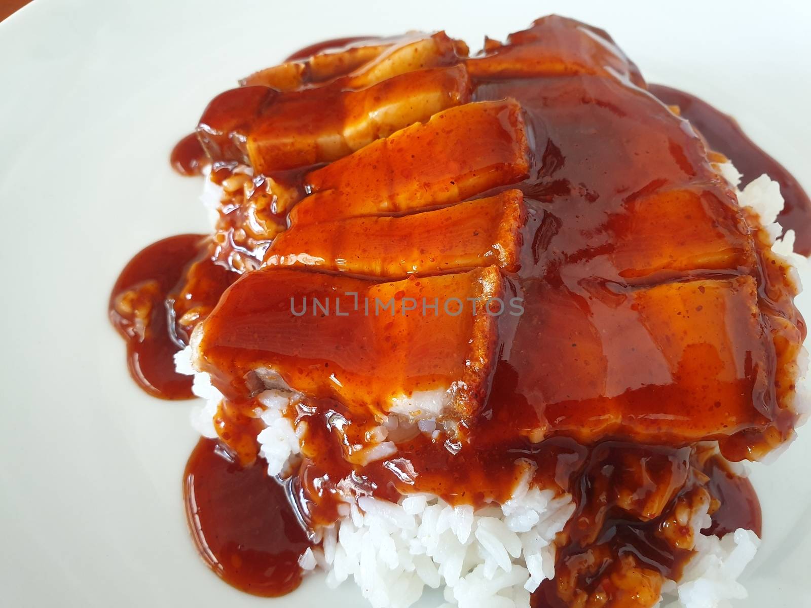 Barbecued red pork in sauce with rice and cucumber served in dish on wood table in Thai restaurant at Thai street food market at Bangkok Thailand