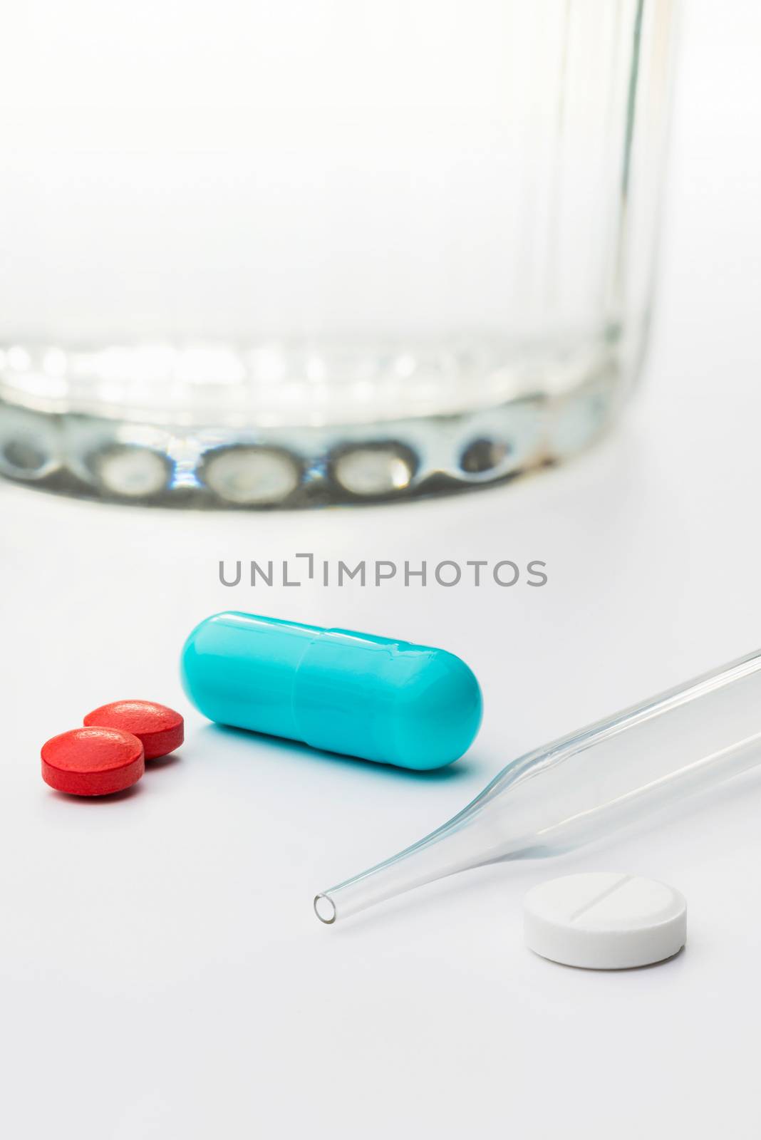 Colored capsules and pills, with a glass of water and a dropper