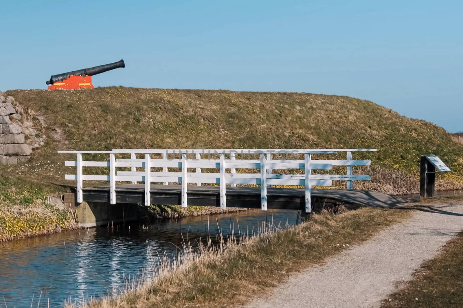A wooden bridge over a small river. A gun on a hill. Open-air museum