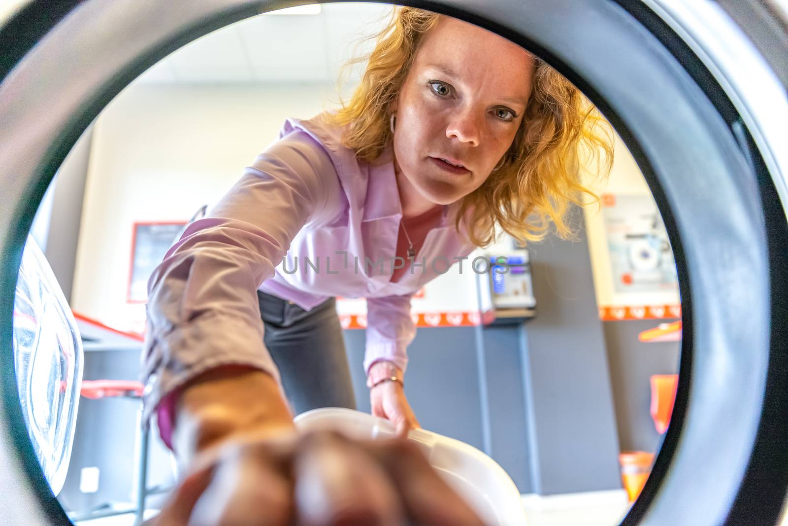 view from the washing machine of a woman inserting clothes into a drum.