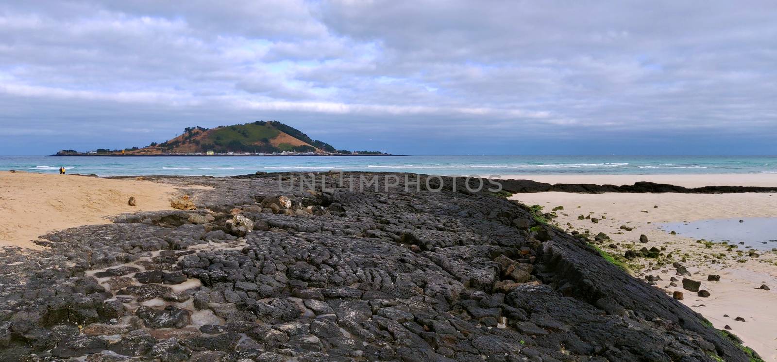 Jeju black volcanic rock on beach with mountain and sea in Jeju Island, South Korea