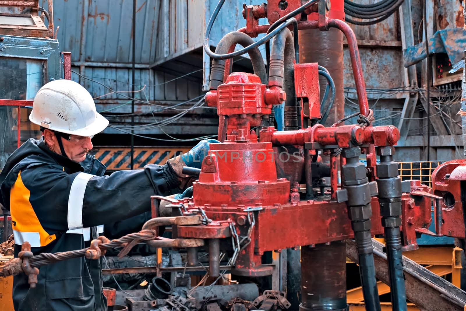 A working oil driller is engaged in spinning pump pressuring pipes on the well. by DePo