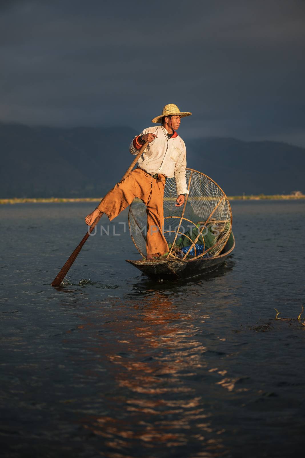 Inle Lake, Myanmar - January 28, 2016 : Burmese fisherman fishing on a traditional bamboo boat with a handmade net early in the morning at sunrise.