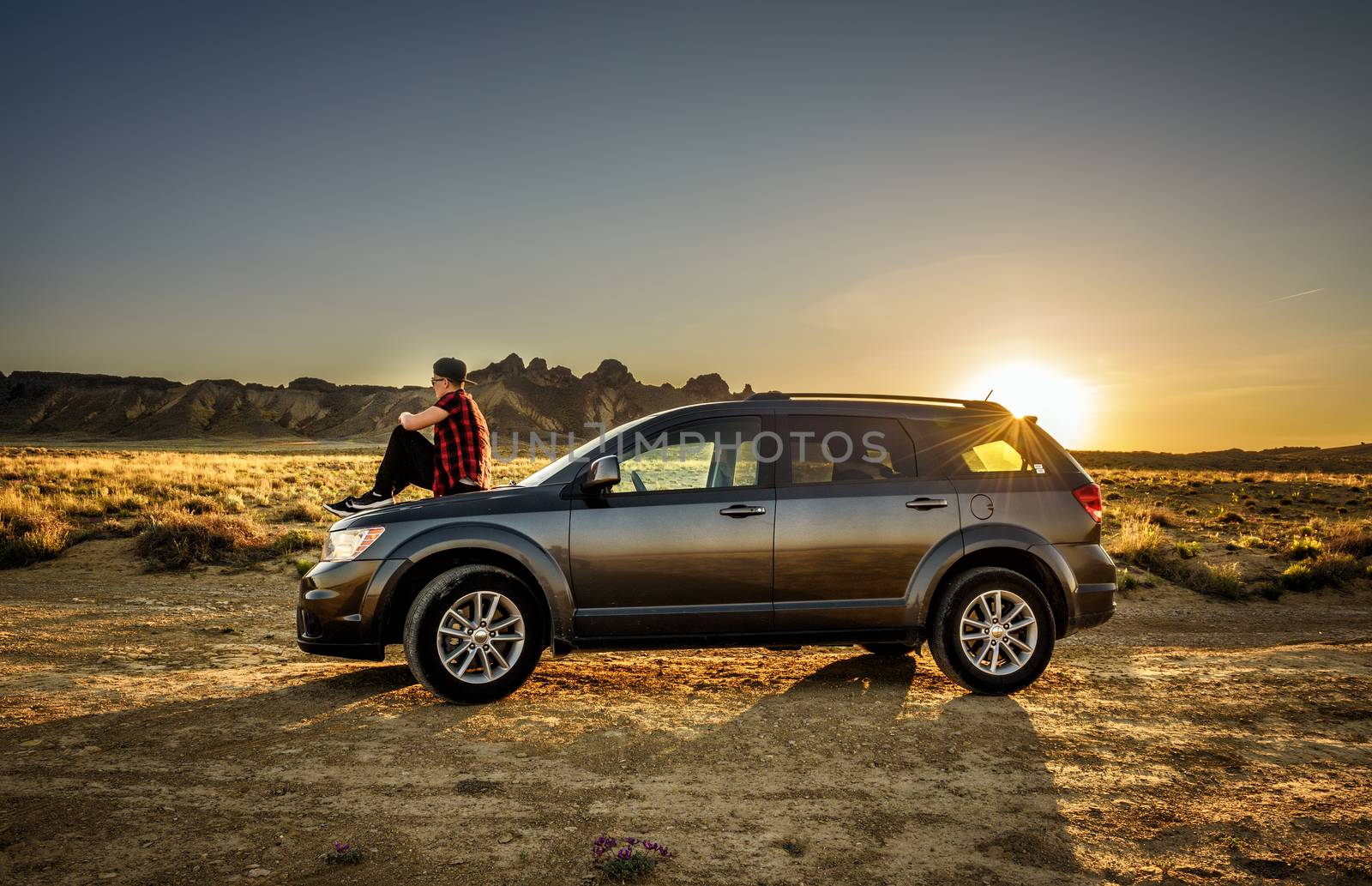 Shiprock, New Mexico, USA - May 14, 2016 : Boy enjoys sunset sitting on the hood of his car on a dirt road in the desert of New Mexico.