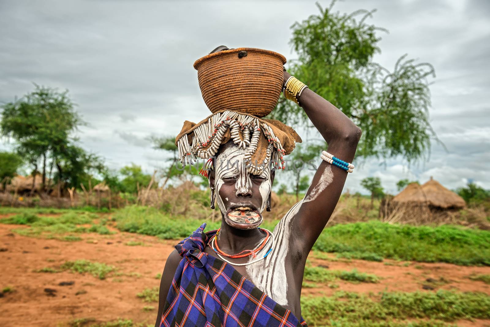 OMO VALLEY, ETHIOPIA - MAY 7, 2015 : Woman from the african tribe Mursi with big lip plate and with a basket on her head
