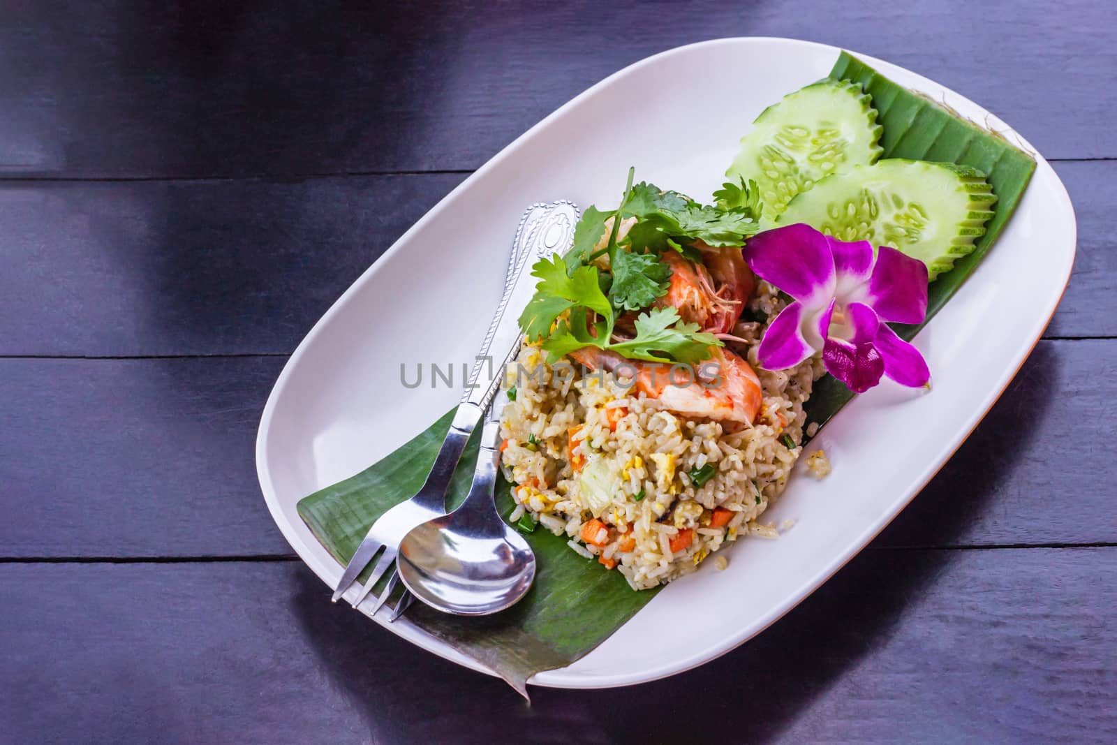 Fried rice with shrimp on the white ceramic dish decorated with orchid put on dark wooden table.
