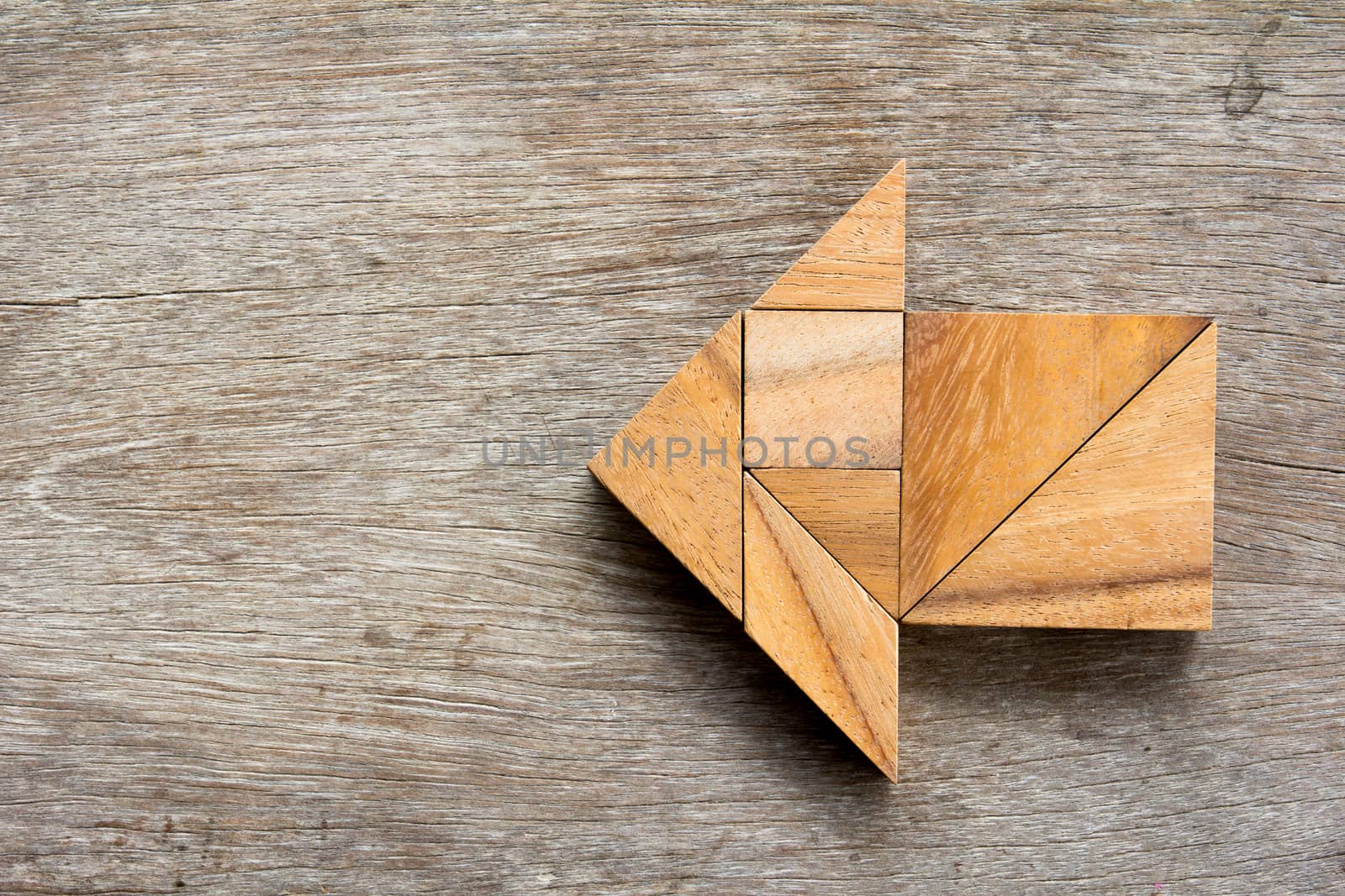 Tangram puzzle in arrow shape on wooden background
