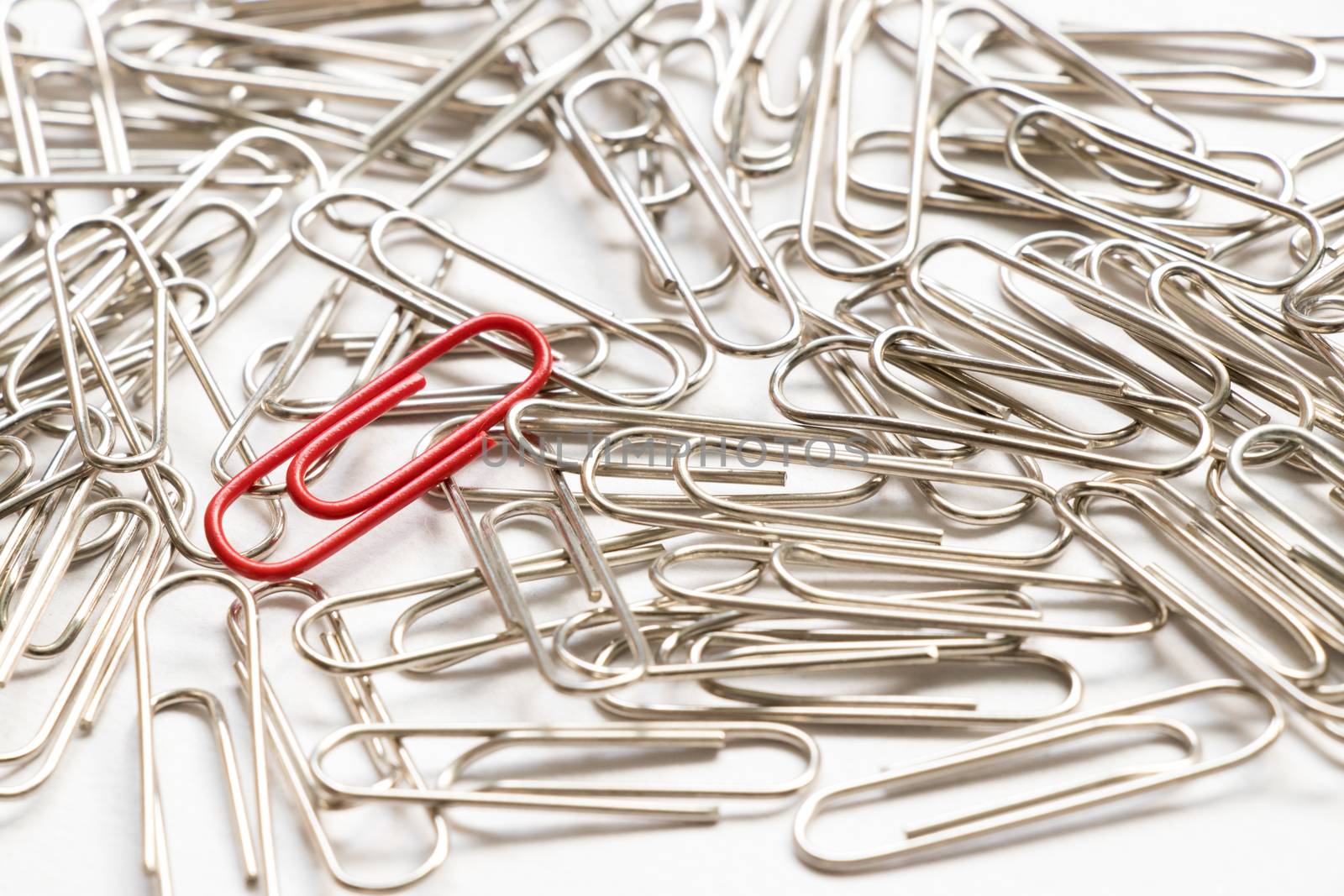 Red paper clip show different from the others on white background