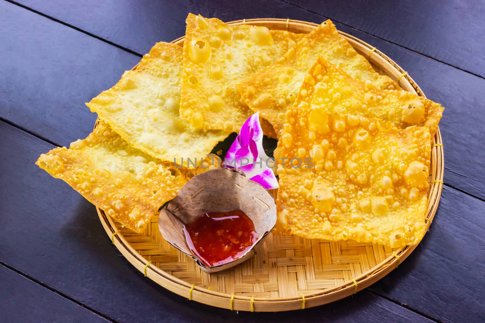 Yellow fried dumplings and a cup of sauce on a bamboo dish at decorated with orchid placed on the table dark wood. by prapstock