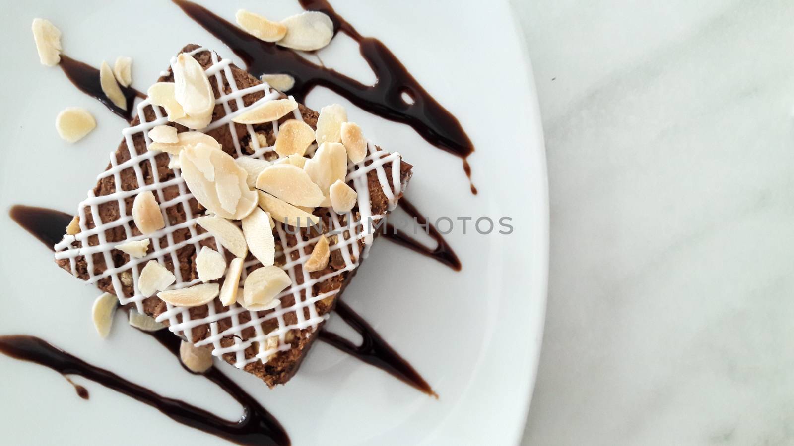Top view of chocolate brownie with sliced almond on white plate background