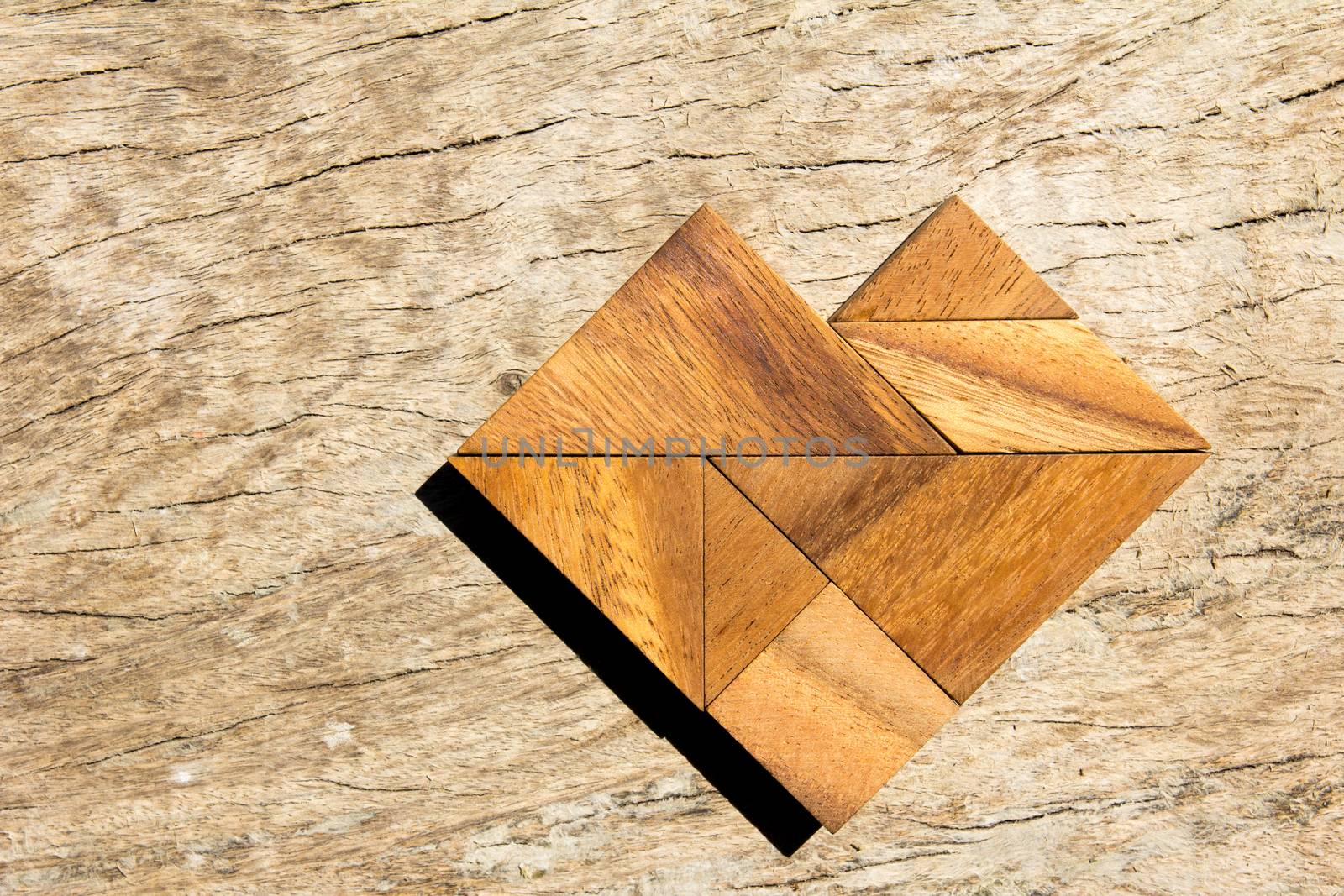 Tangram puzzle in heart shape on wooden background