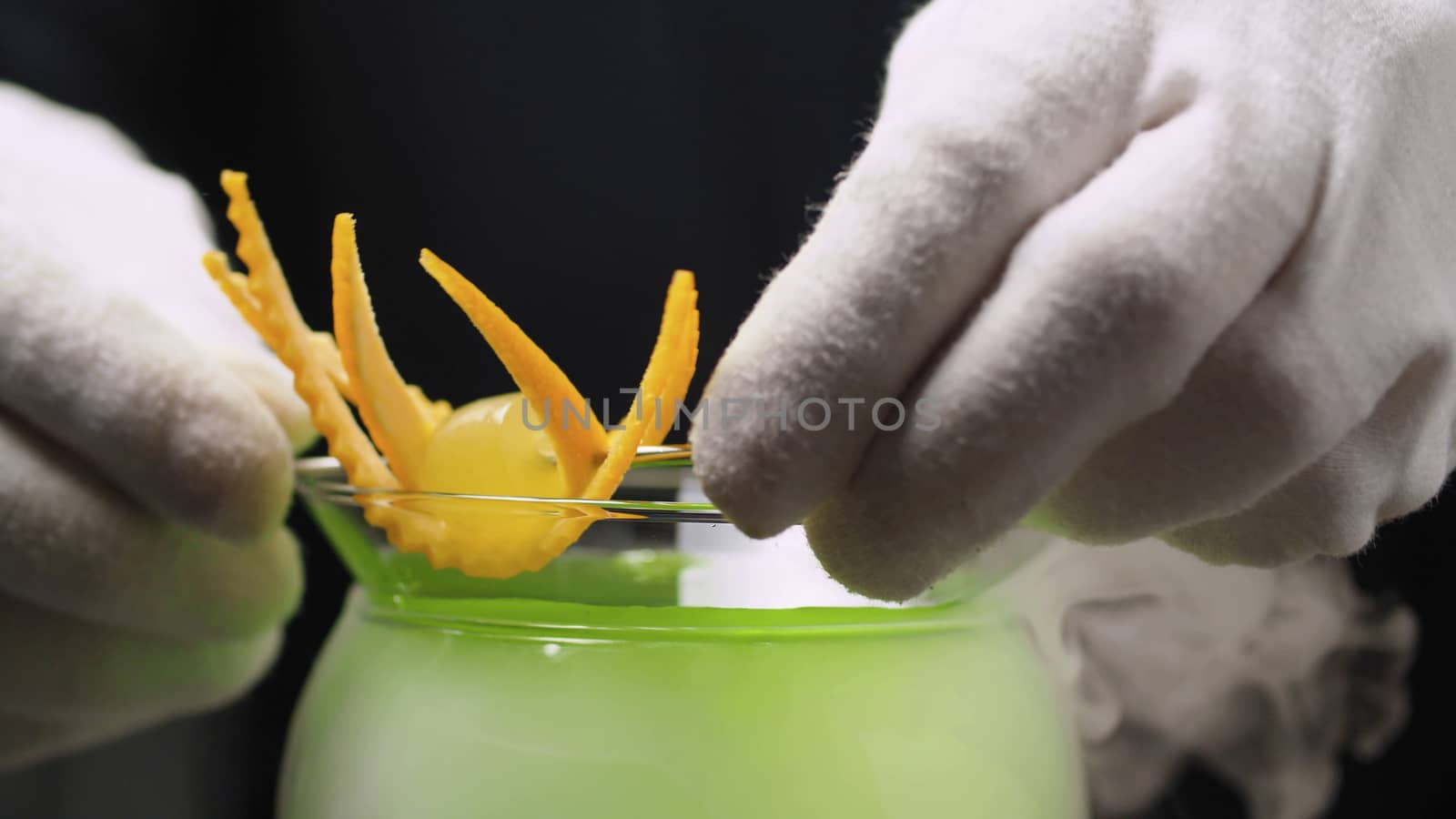 Cooking Grape Martini Cocktail. Close up bartenders hands decorating with orange zest. The glass is wrapped in steam