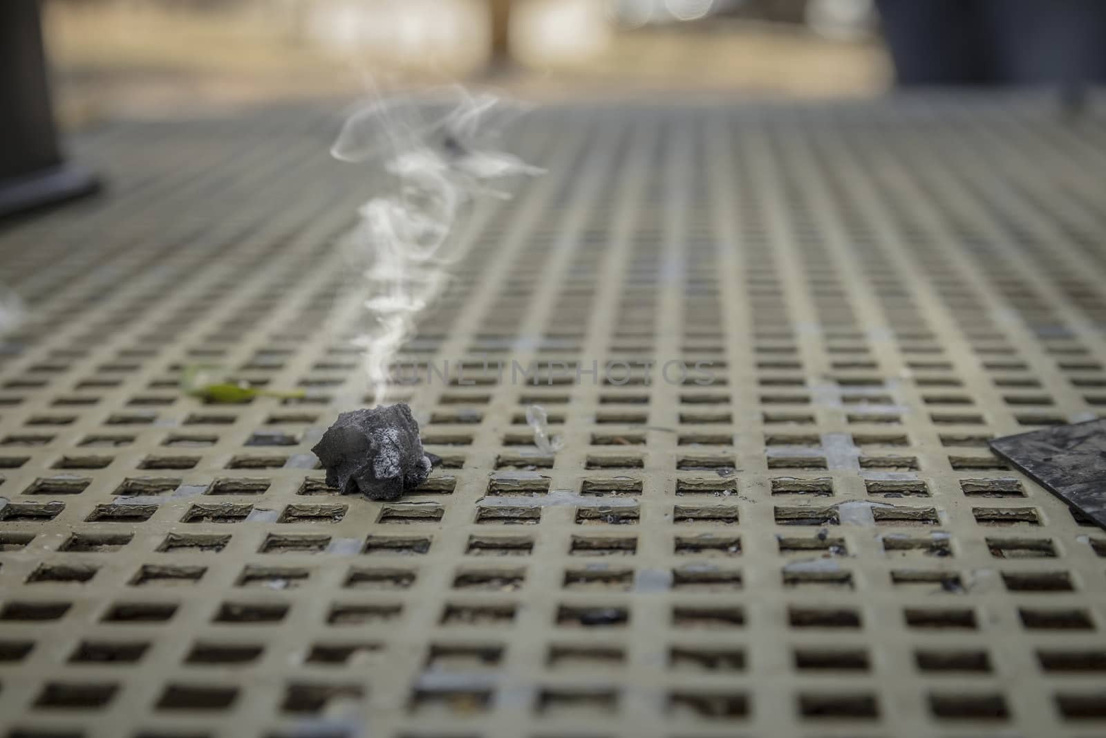 Smoke emitted from a piece of burnt wood coal on a metal table. Close up with selective focus.