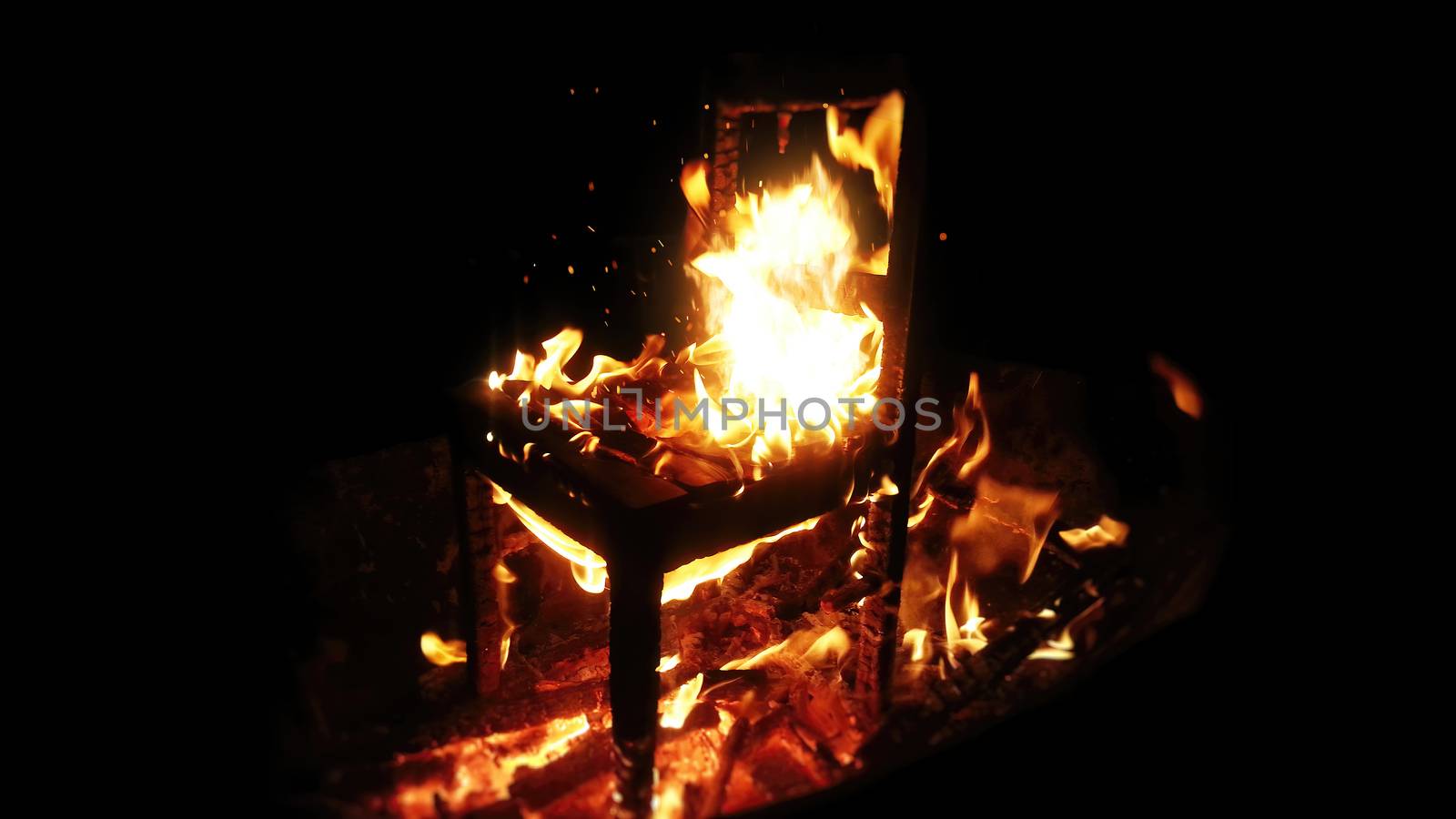 Wooden chair burning inside the bonfire. Close up on sparks rises from the fire with heatwaves at night. A horror concept of a demonic ritual or devil and demons religious worship.