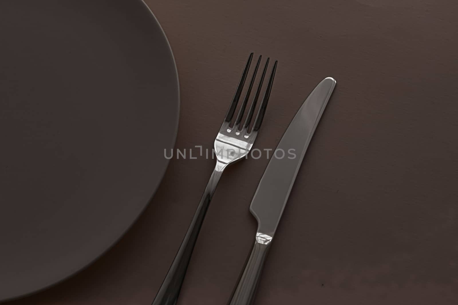 Empty plate and cutlery as mockup set on dark brown background, top tableware for chef table decor and menu branding by Anneleven