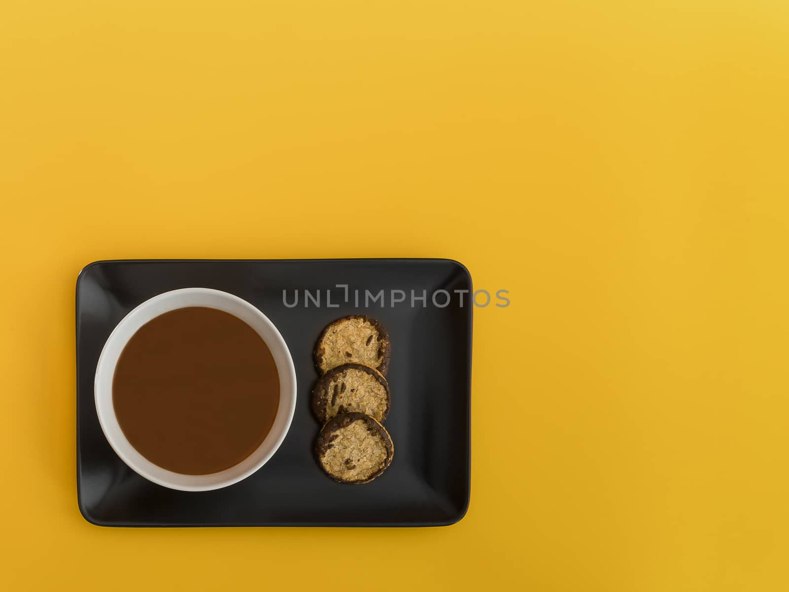 Chocolate bowl on a black tray. Yellow background. Minimalist image from above with space available to copy text. Top view.