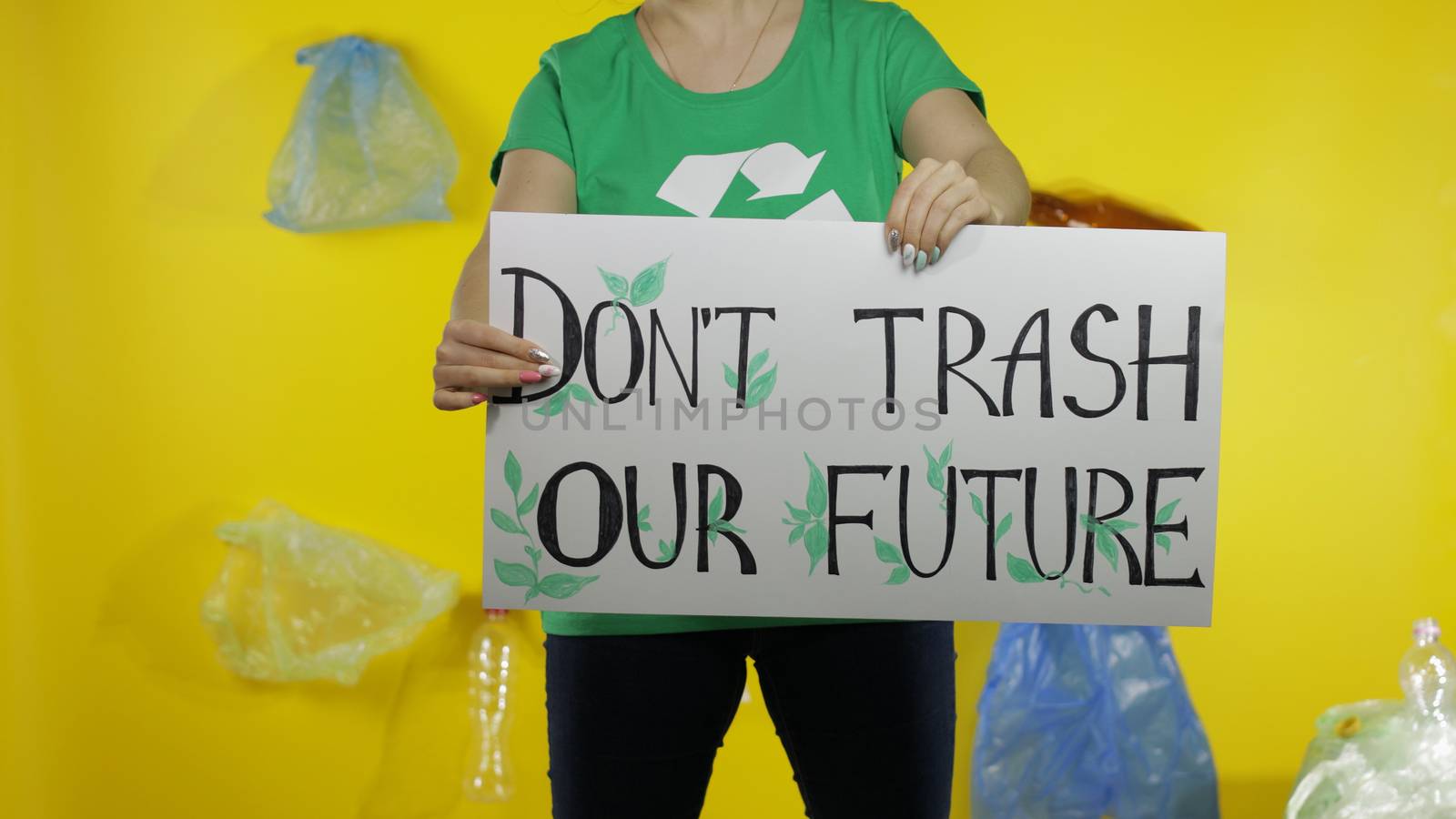 Unrecognizable woman volunteer in t-shirt with recycle logo holding protesting message poster Don't Trash Our Future. Background with cellophane bags, bottles. Environment trash plastic pollution