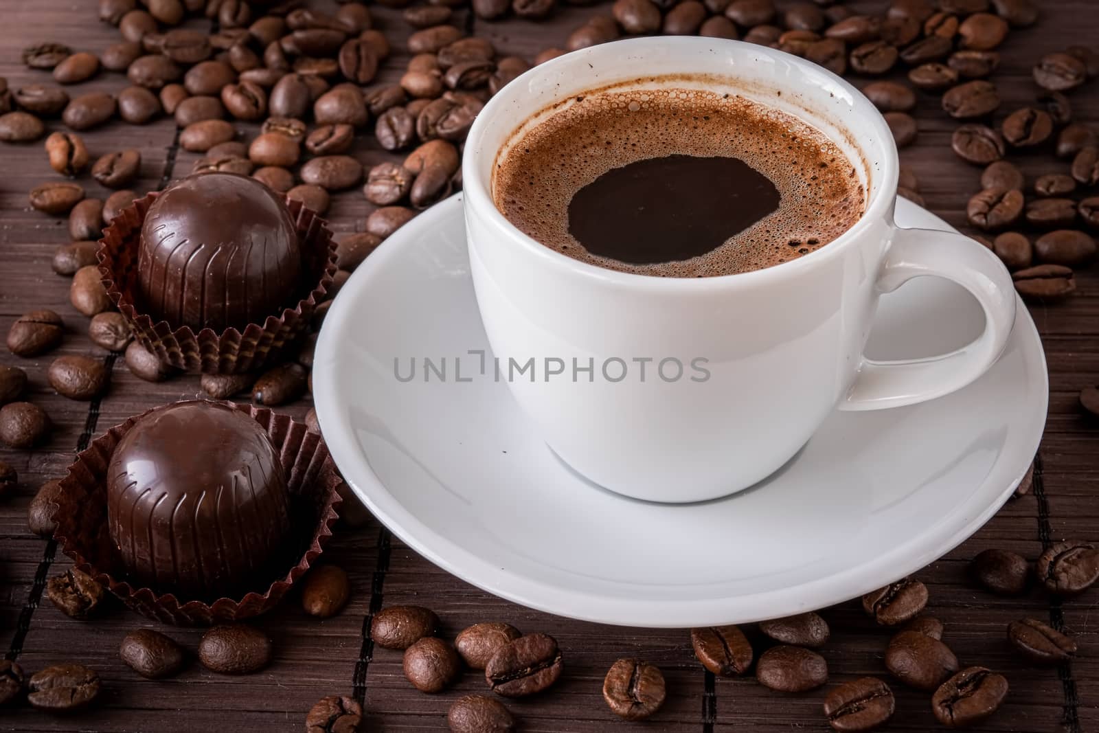 Cup of hot coffee and a scattering of coffee beans on a bamboo serving napkin.