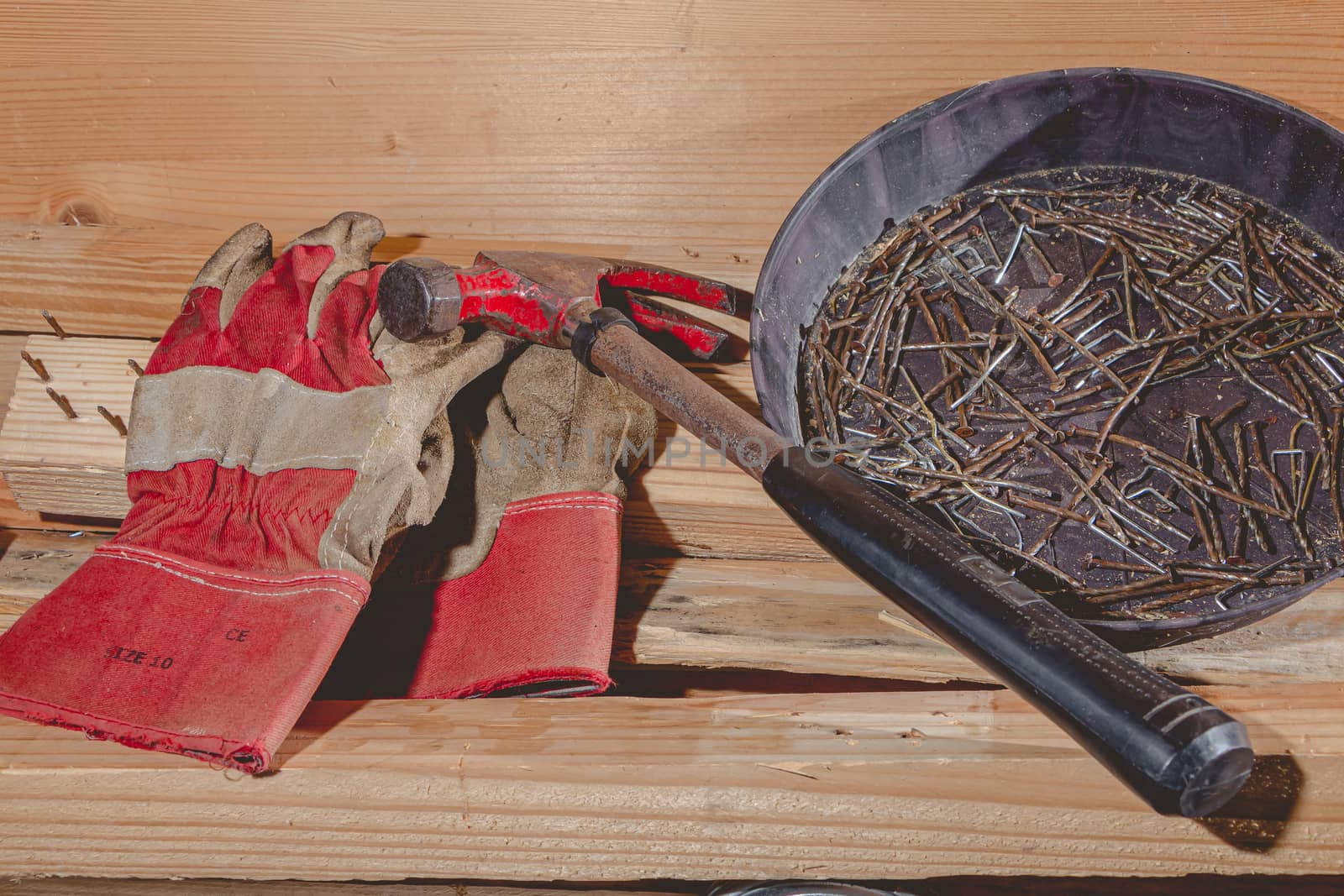 old rusty hammer and construction gloves laid on wooden board in studio