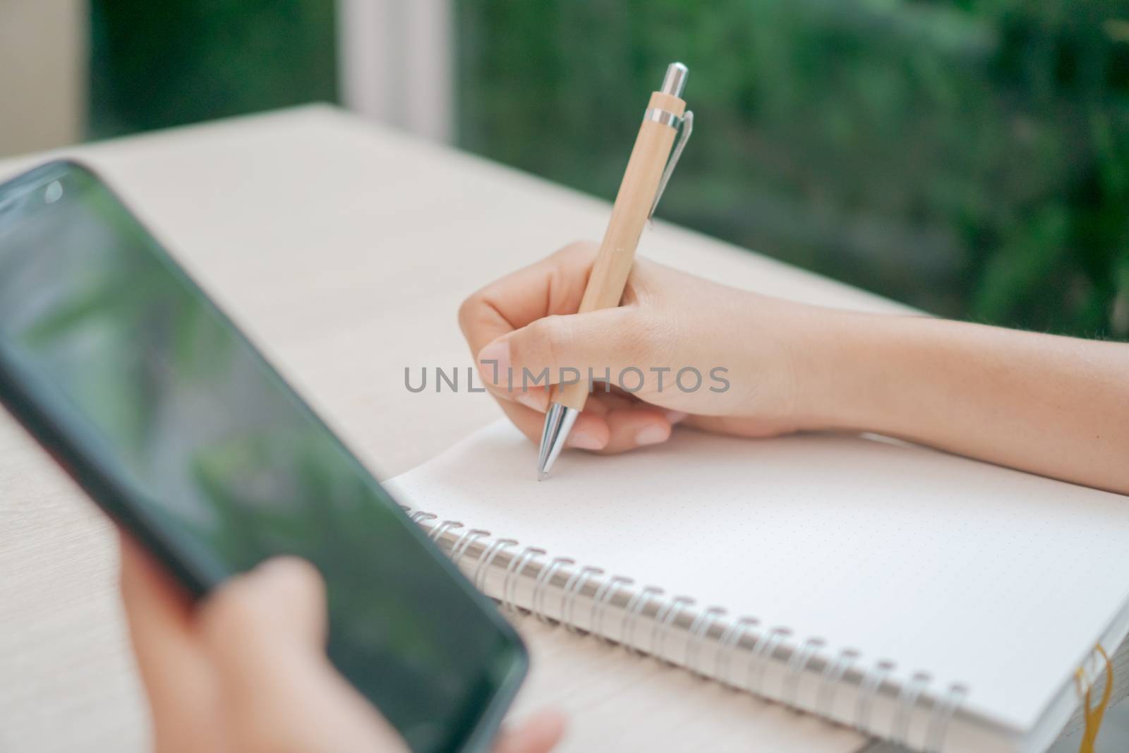 Woman hand write down in white memo notebook for take a note not to forget, to do list or plan for work in future on work table. by Suwant