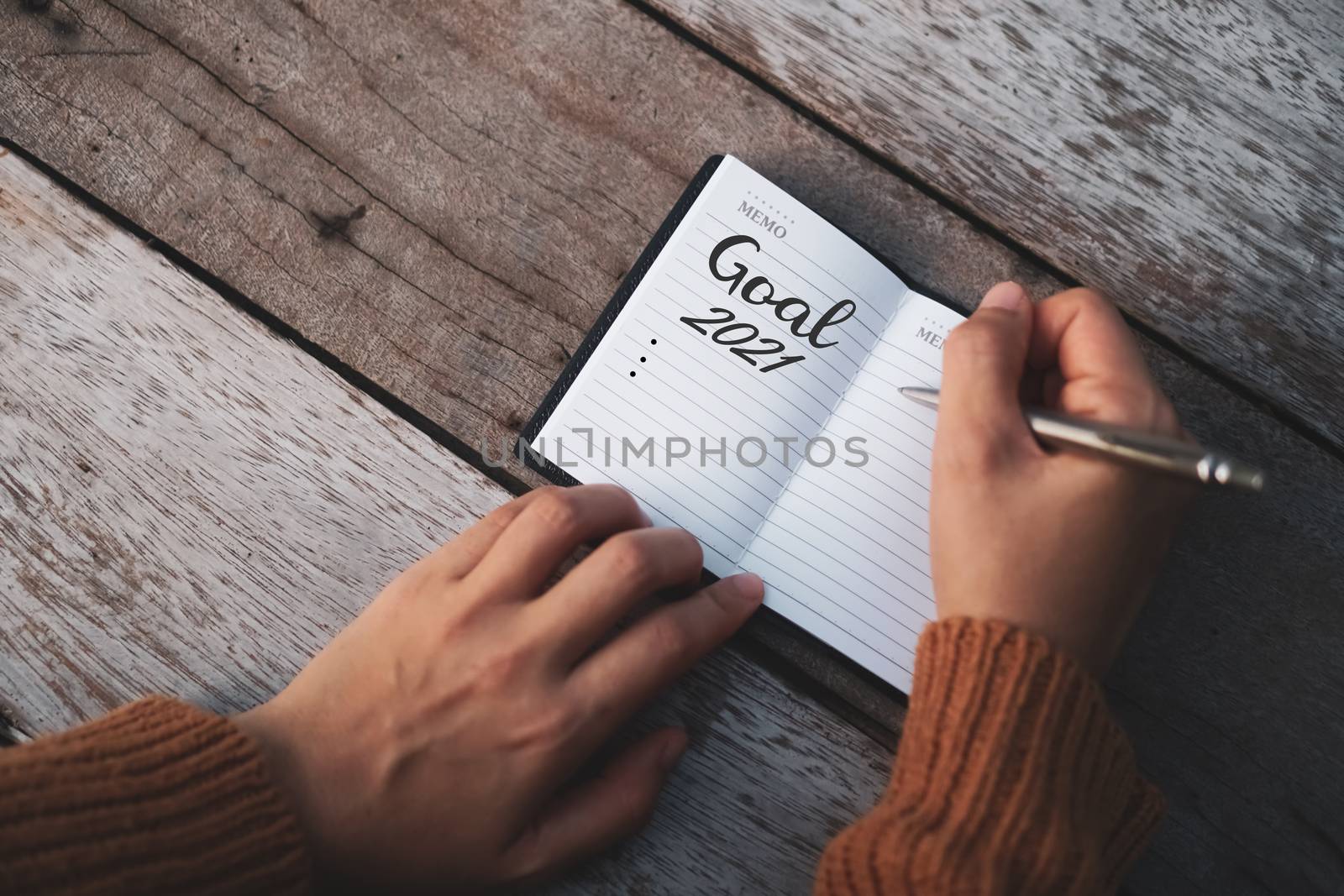 Top view of  goal for 2021 on notebook paper with pen on table. by Suwant