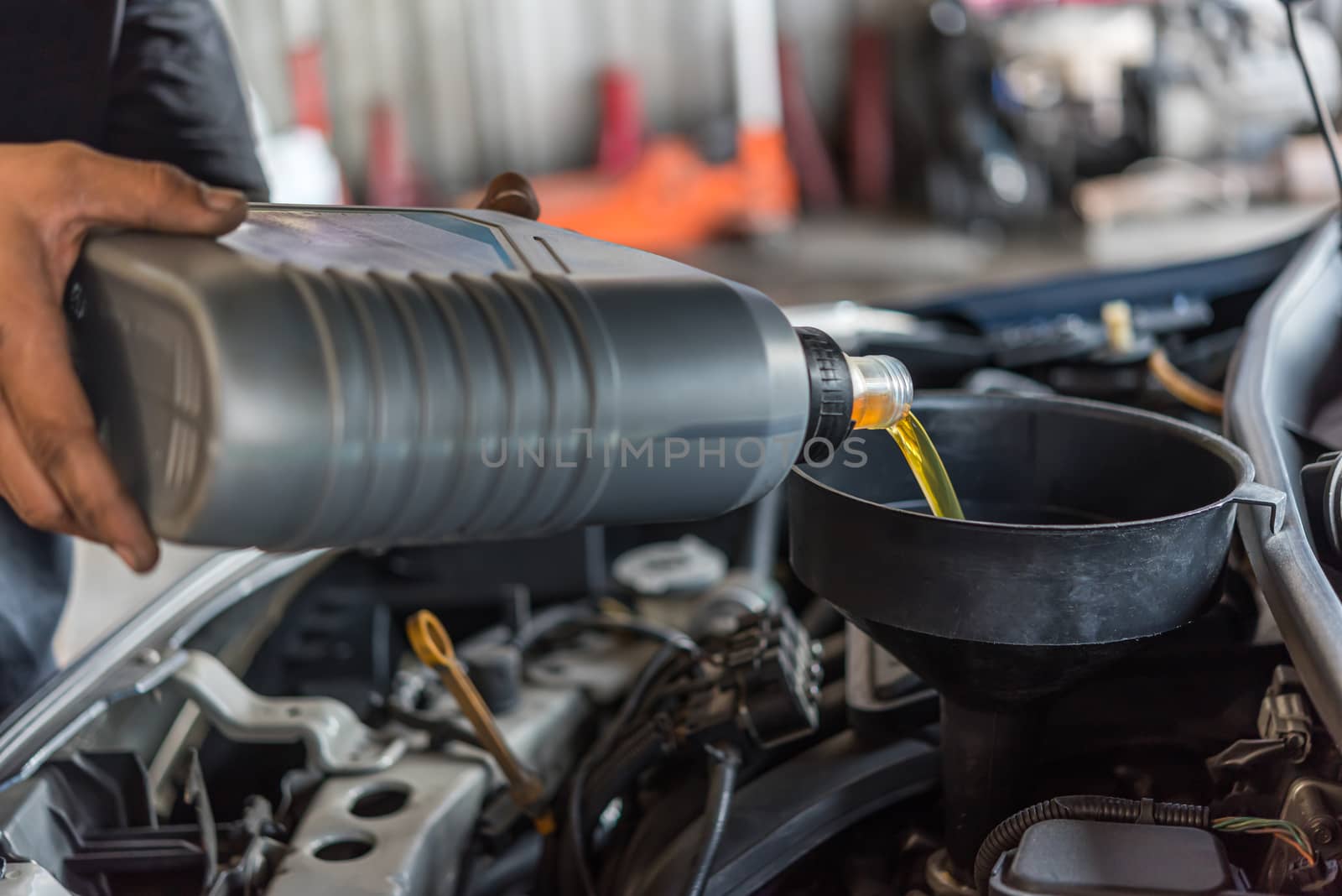 Car mechanic fills a fresh lubricant engine oil by PongMoji