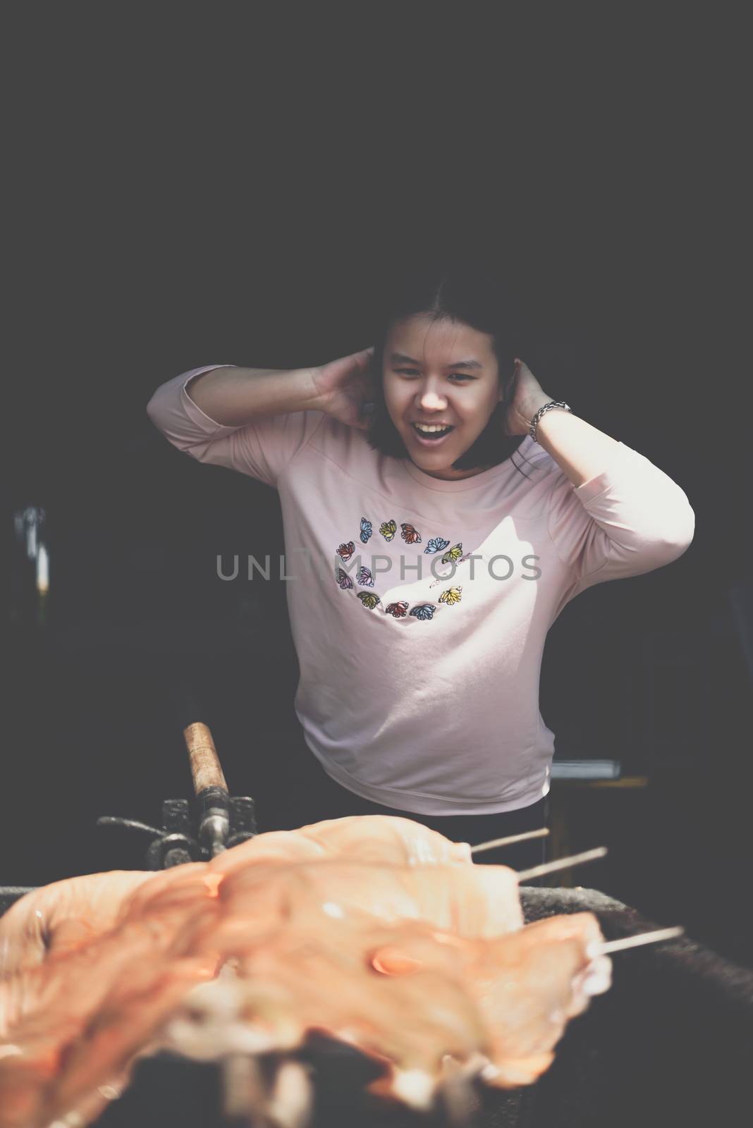 Asian woman chef cooking Barbecued Suckling Pig by roasting pork on charcoal for sale at Thai street food market or restaurant in Thailand