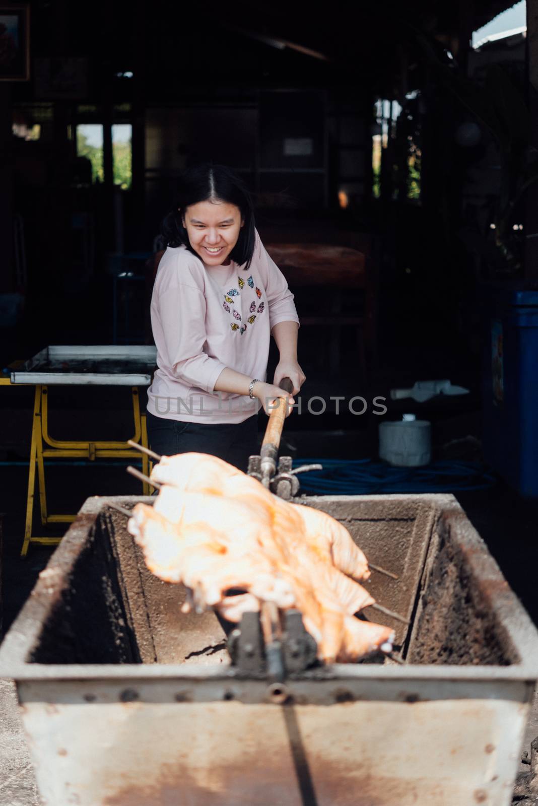 Asian woman chef cooking Barbecued Suckling Pig by roasting pork on charcoal for sale at Thai street food market or restaurant in Thailand