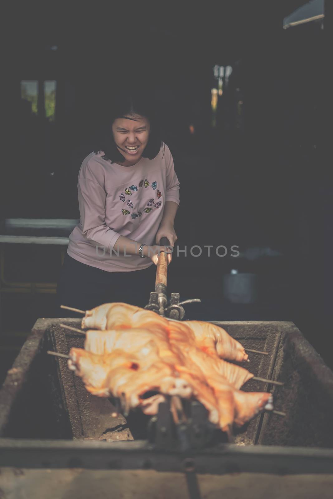 Asian woman chef cooking Barbecued Suckling Pig by roasting pork on charcoal for sale at Thai street food market or restaurant in Thailand