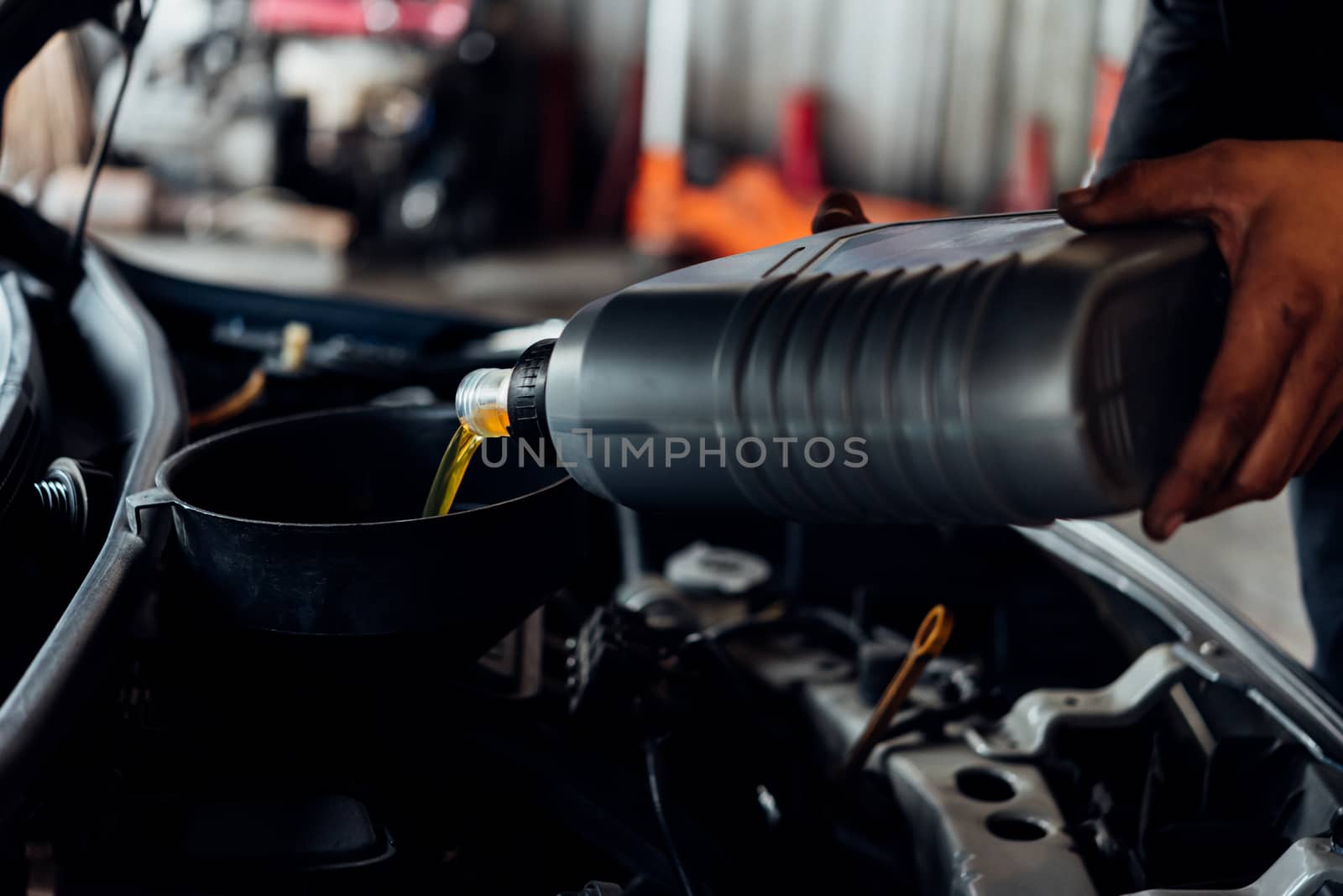 Car mechanic or serviceman fills a fresh lubricant engine oil at car garage for repair or maintenance a car