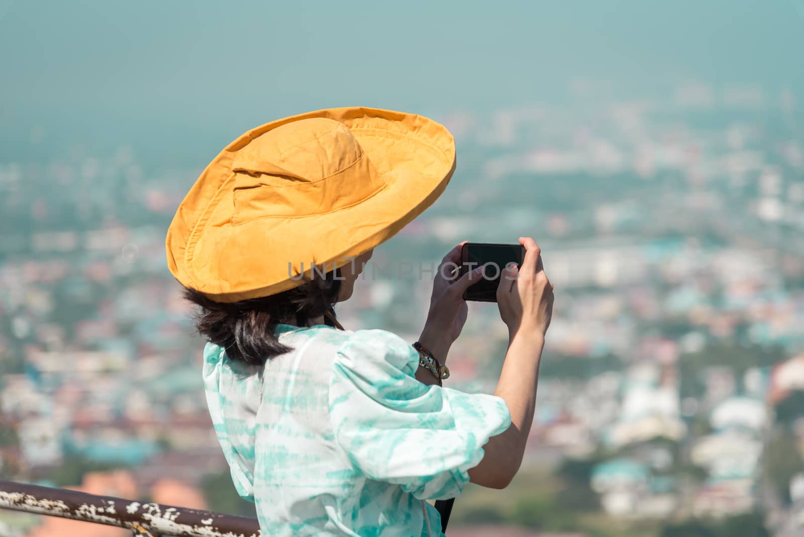 Asian pretty cute woman with hat relax and use smartphone at seaside city landscape viewpoint on mountain with happy and freedom emotion in concept travel, vacation, leisure in life