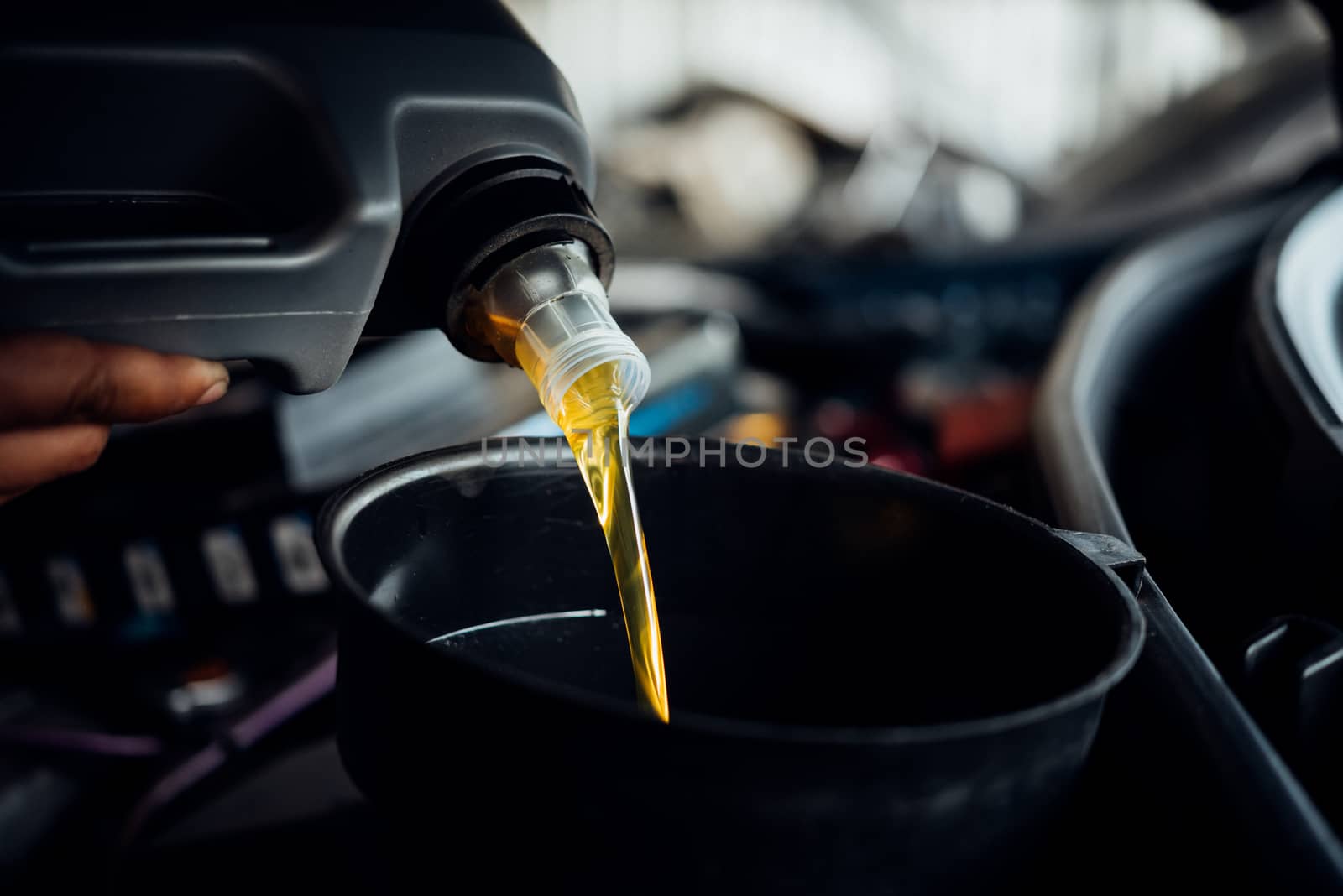 Car mechanic fills a fresh lubricant engine oil by PongMoji