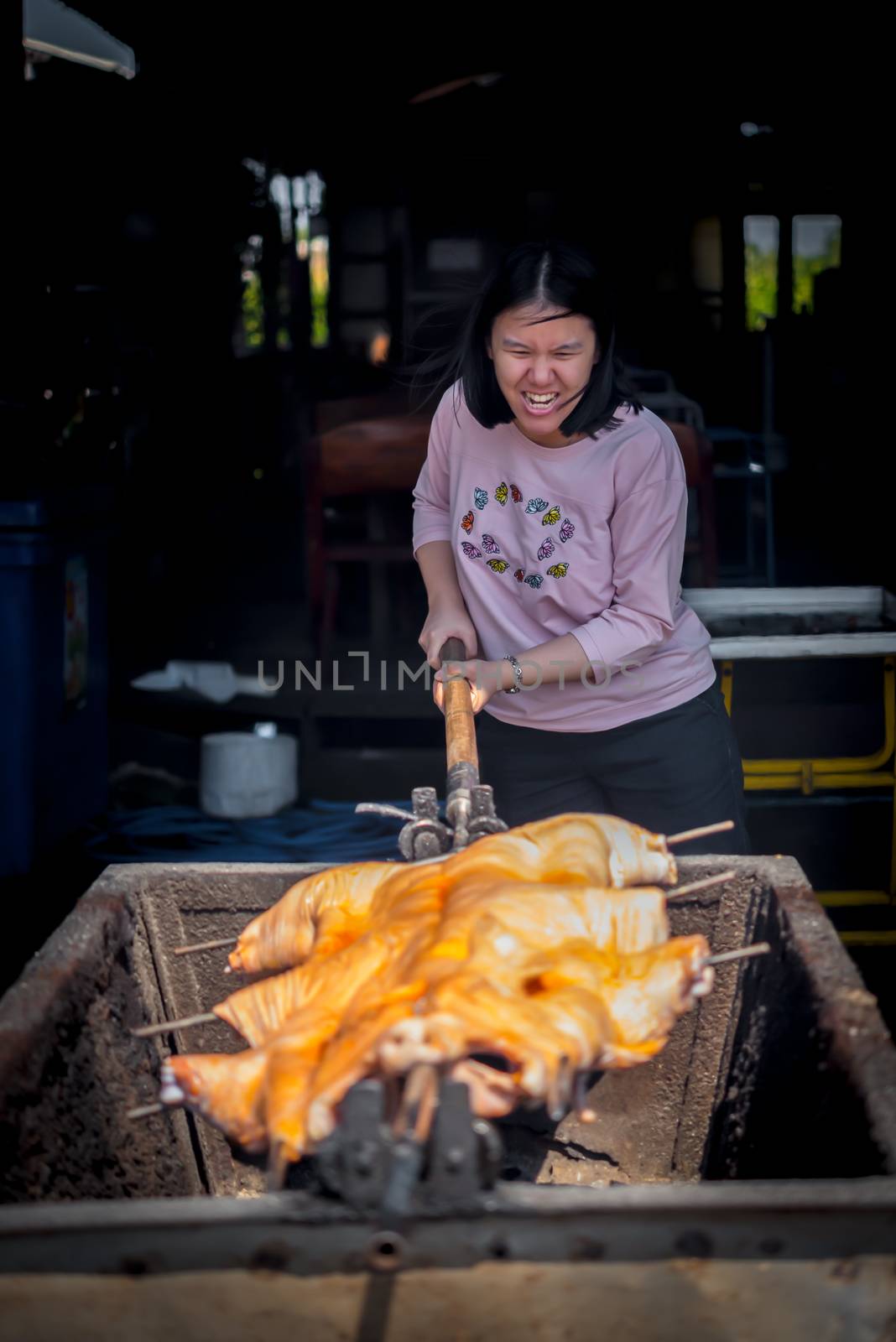 Asian woman chef cooking Barbecued Suckling Pig by roasting pork on charcoal for sale at Thai street food market or restaurant in Thailand